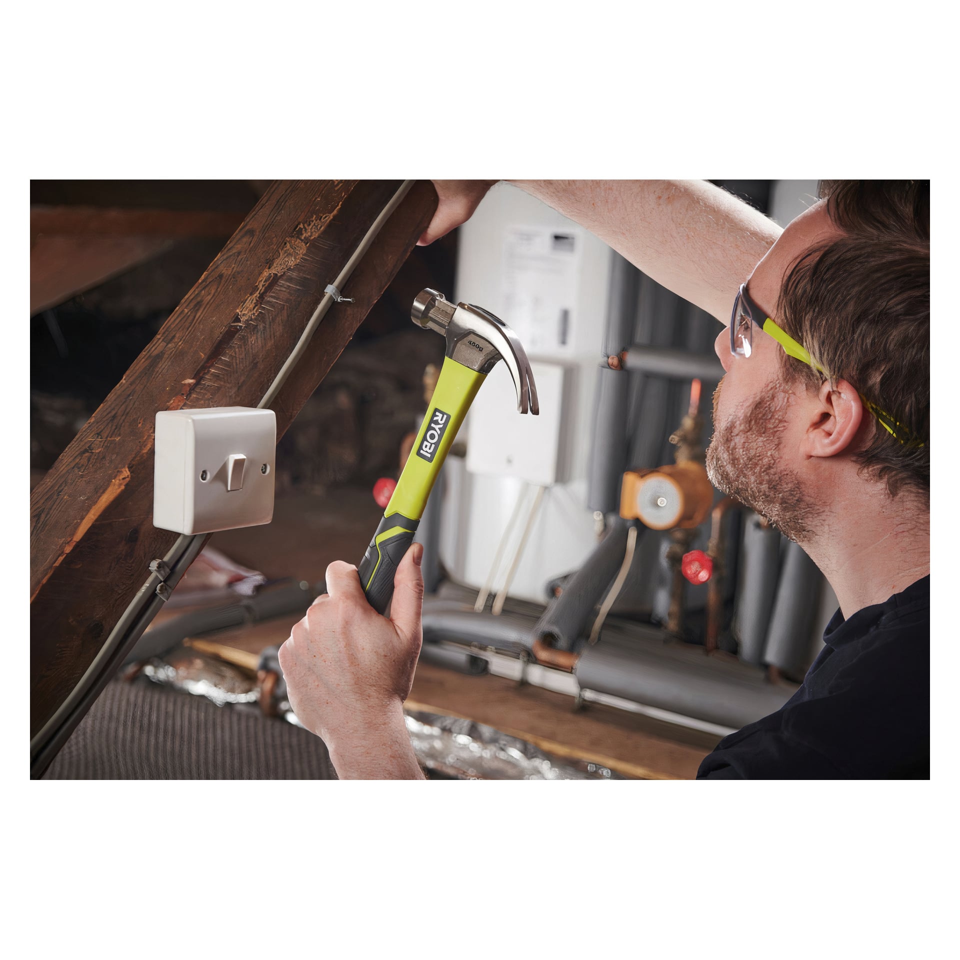 Med skyddsglasögon håller man i en Ryobi Carpenter's Hammer RHHCC450, redo att arbeta nära elledningar och en väggströmbrytare i en ofärdig källare eller teknikutrymme.