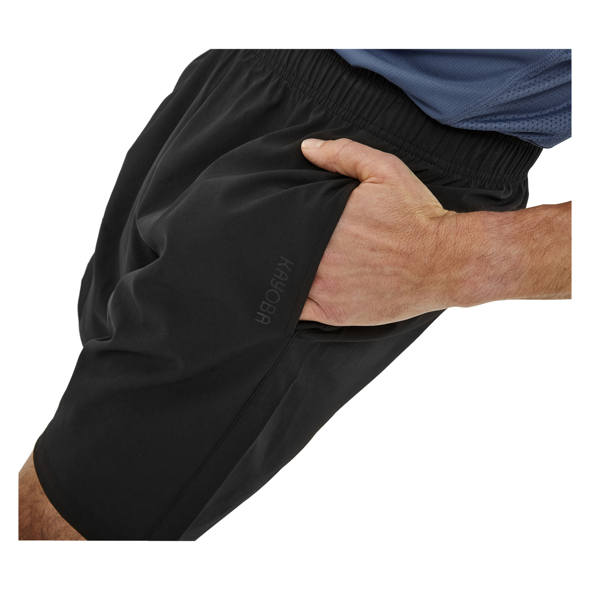 En person klädd i en blå topp och svarta Kayoba träningsshorts för herrar står med höger hand nedstoppad i shortsfickan, som visar en diskret Kayoba-logga bredvid.