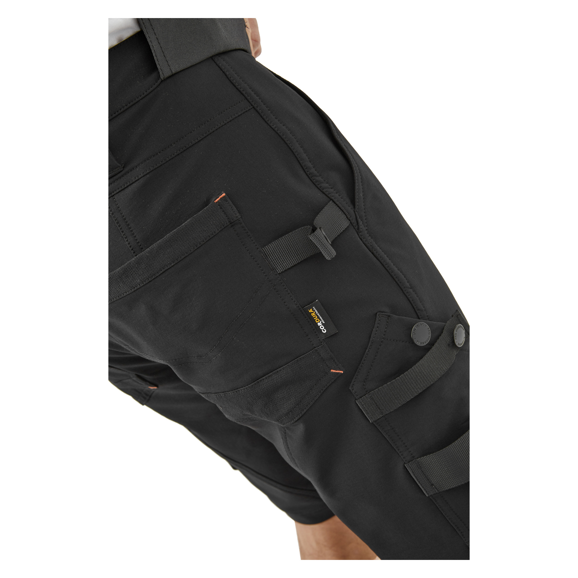 Närbild på en person i svarta Steve-arbetsshorts från Bluewear Pro Workwear, designade med flera fickor, öglor och knappdekorationer. En ficka visar en liten svart och gul etikett.
