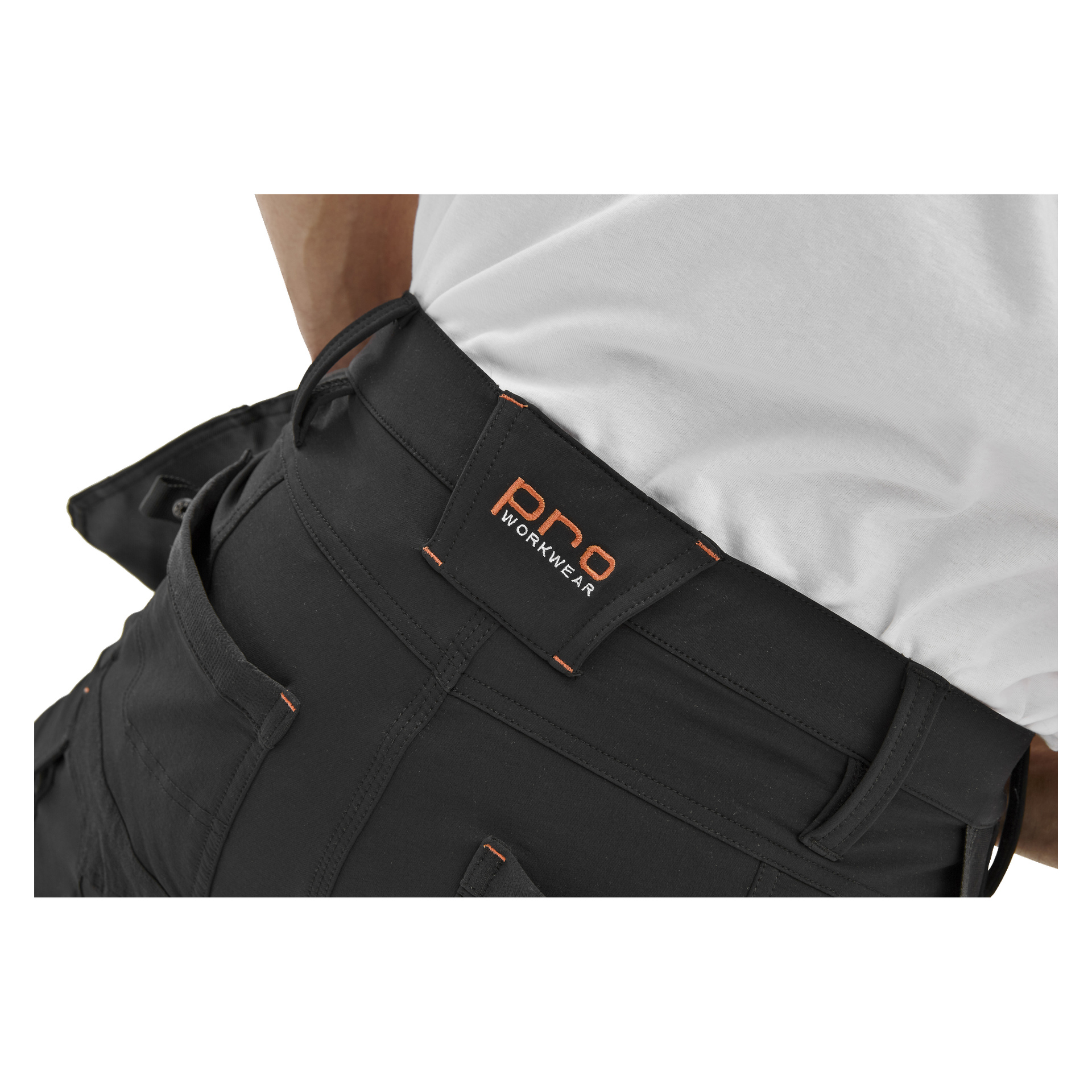 Närbild på en person klädd i Bluewear Pro Workwear herrshorts från Steve och en vit skjorta. De svarta shortsen har en framträdande svart etikett med orange sömmar där det står "PRO WORKWEAR", tillsammans med flera fickor och bältesöglor.