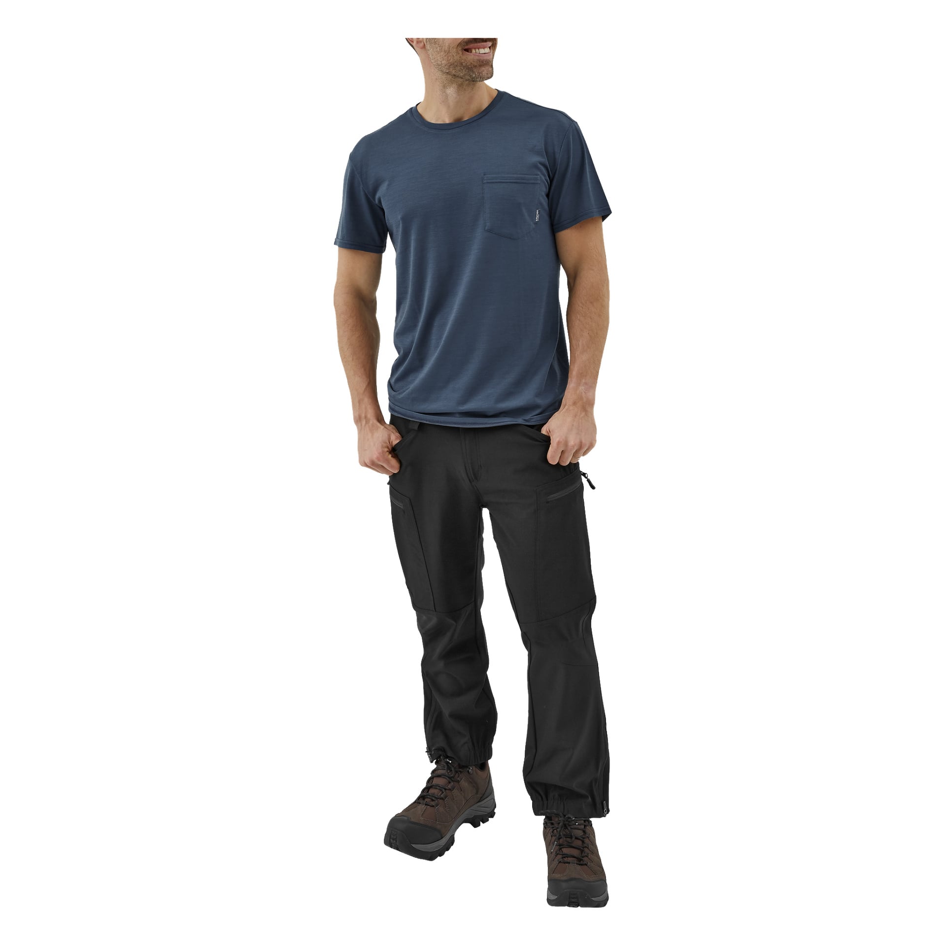En man är klädd i en blå kortärmad t-shirt med fickor, svarta Kayoba Outdoor herrbyxor från Östanå med dragkedjasförsedda cargofickor och bruna vandringskängor. Han ler och tittar åt sidan.