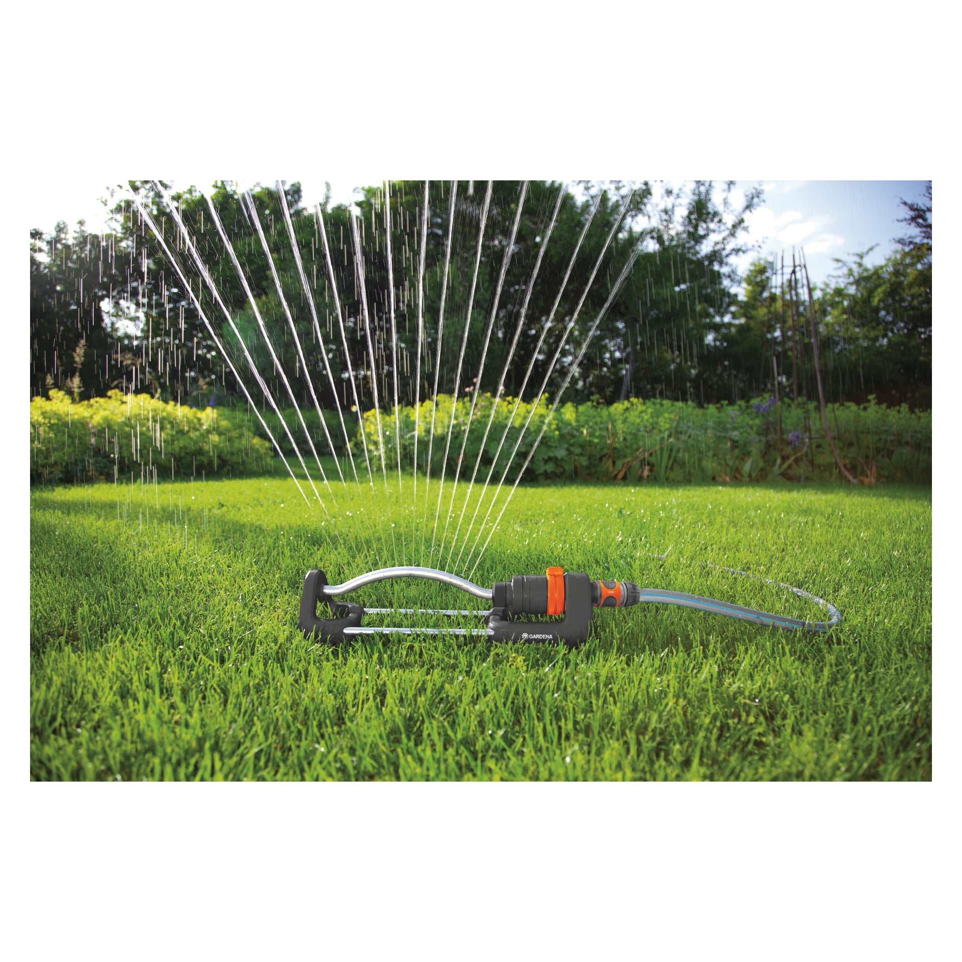 Gardena Water Sprinkler Aqua S fördelar flera vattenstrålar över frodigt grönt gräs i en trädgård, med olika träd och växter i bakgrunden. En slang är ansluten till sprinklern.