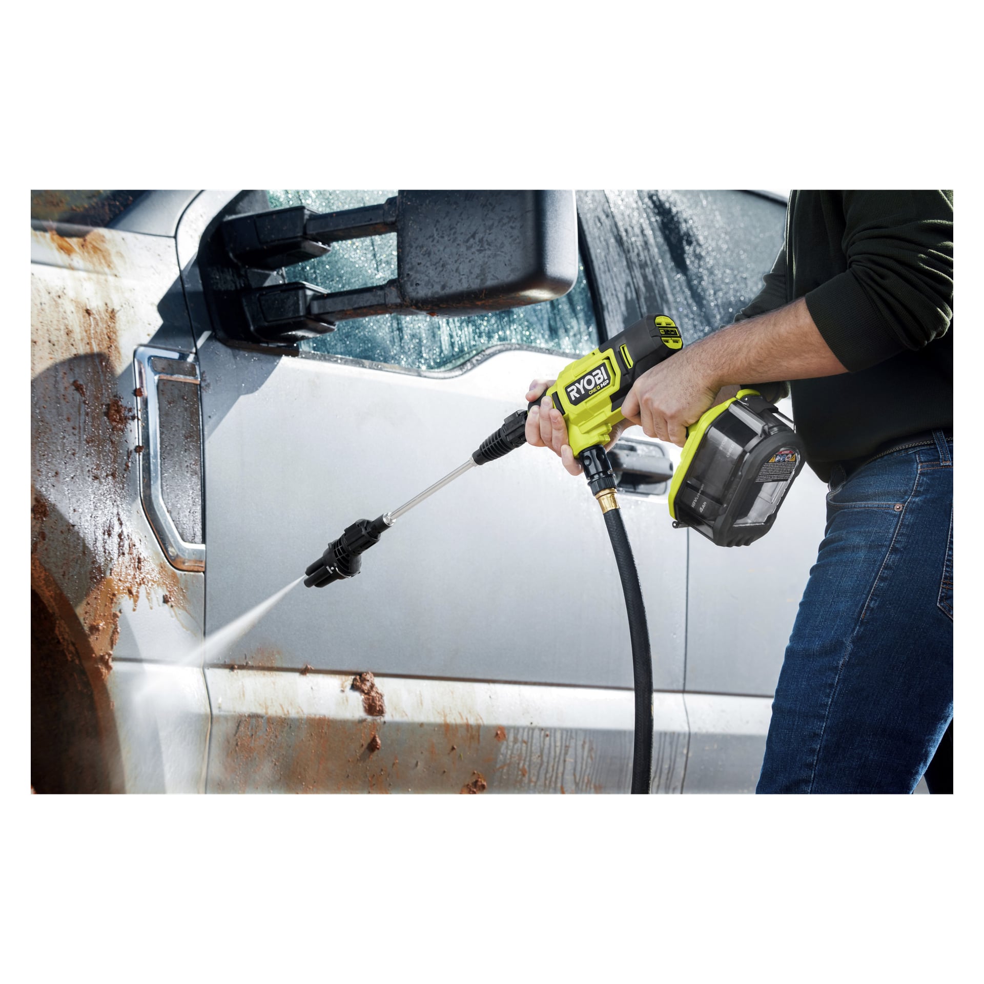 Någon använder Ryobi One+ HP batteridrivna medelhöga högtryckstvätt RY18PWX41A-0, och riktar sin stråle mot en silverfärgad lastbilsdörr för att ta bort lera. Vattenstrålar från munstycket och sköljer bort lite smuts medan lerfläckar fortfarande syns på lastbilen.