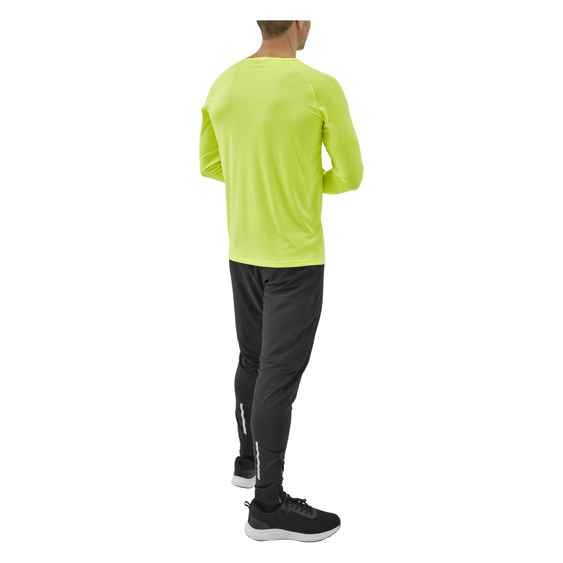 En person står med ryggen mot betraktaren, klädd i en neongul långärmad funktionell topp från Kayoba, tillsammans med svarta joggingbyxor med reflekterande remsor och svarta sportskor.