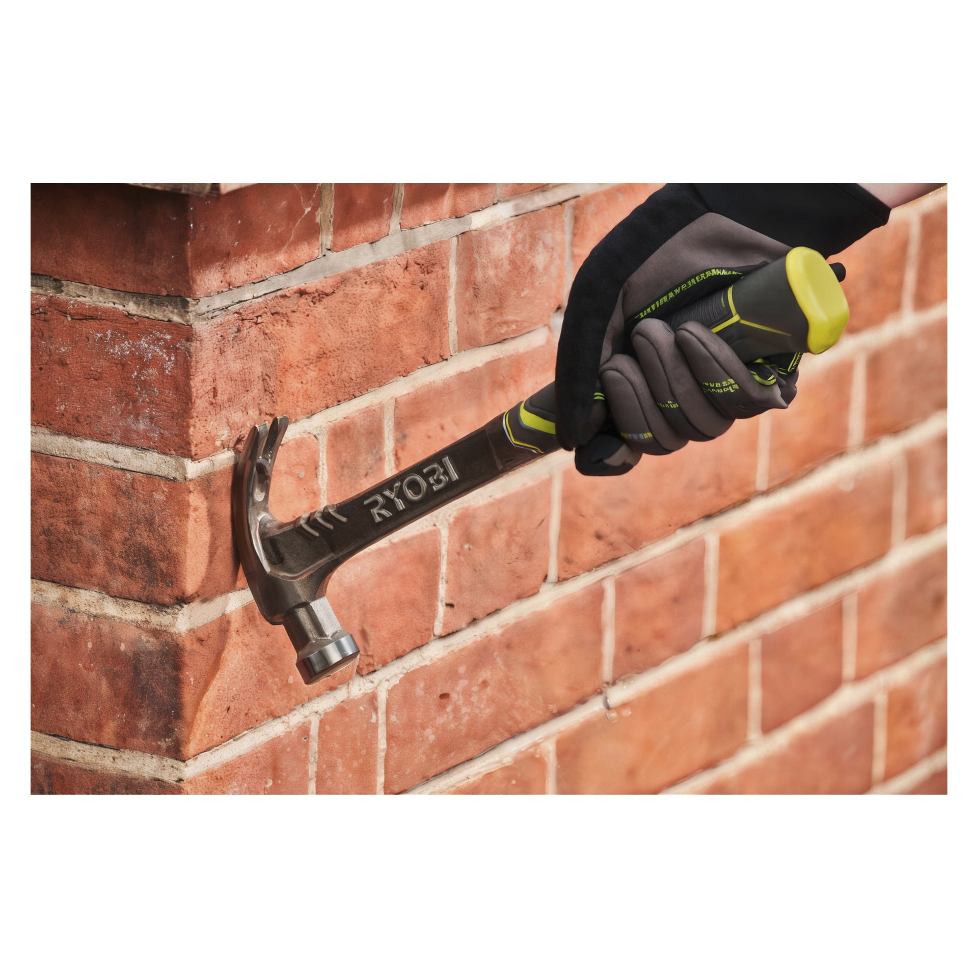 En hand med handske greppar en Ryobi-snickarhammare, redo att dra bort en spik från en röd tegelvägg. En del av personens arm är synlig, och hammaren visar tydligt varumärket Ryobi.