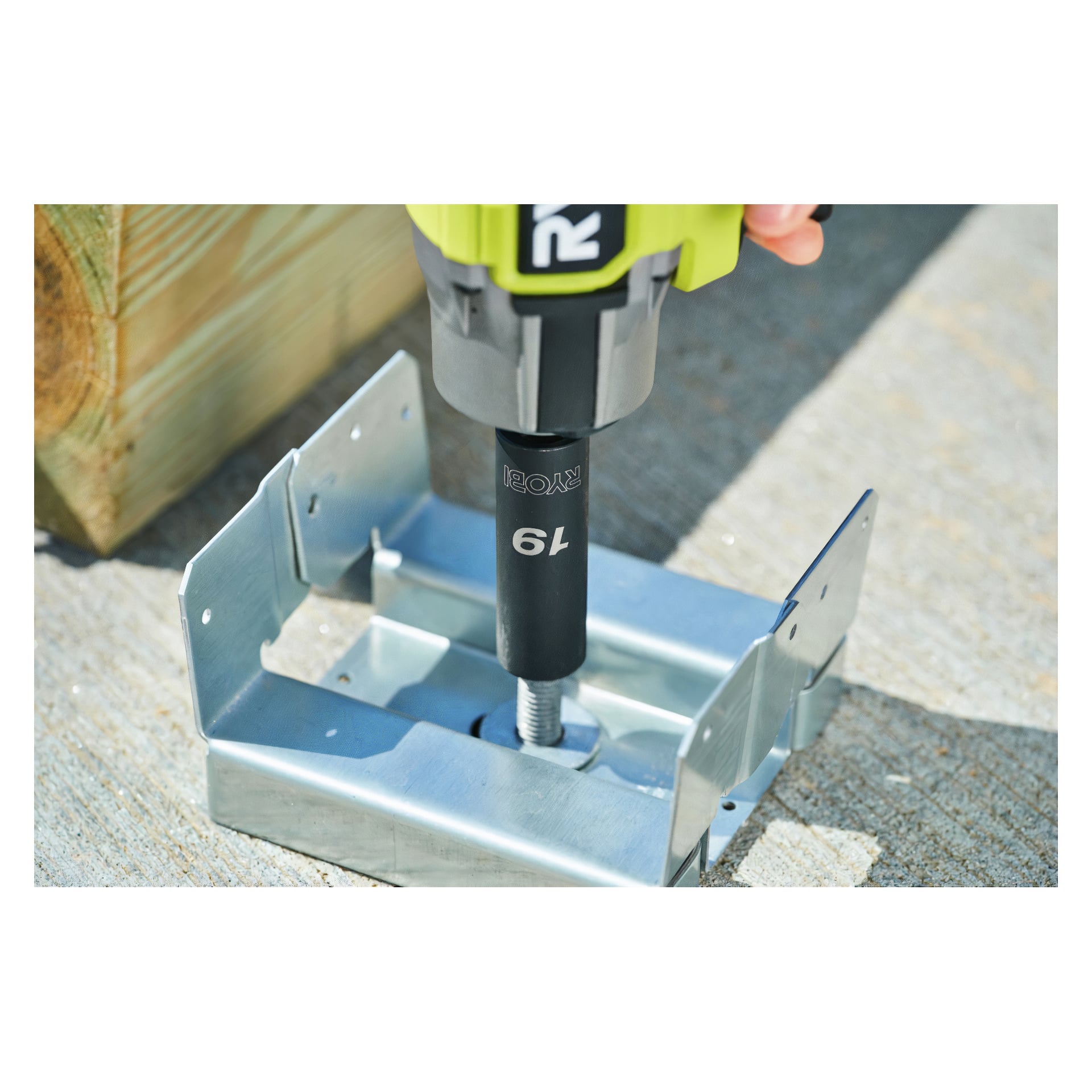 Någon arbetar med Ryobi Socket Set RHDIS3PC (3-delad), där en 19 mm hylsa monteras på ett sladdlöst verktyg för att fästa en stor bult i ett metallfäste monterat på betong. En träbit syns i bakgrunden.