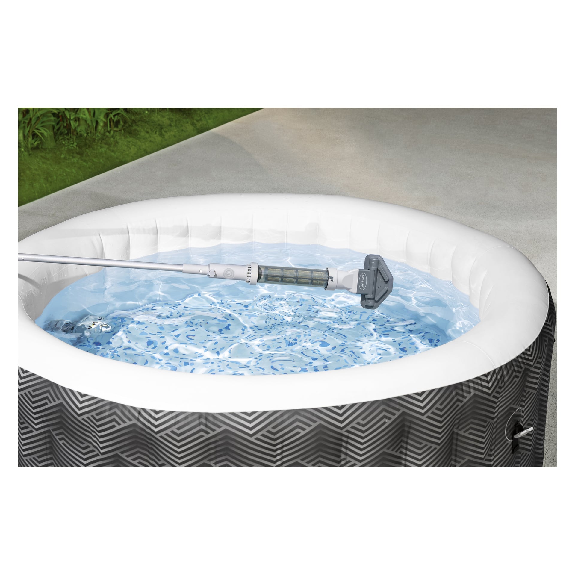 En rund Bestway Lay-Z-Spa uppblåsbar bubbelpool med grått och vitt chevronmönster står fylld med klart vatten. En Bestway uppladdningsbar pooldammsugare för Lay-Z-Spa står delvis under vatten. Betong och gräs syns i bakgrunden.