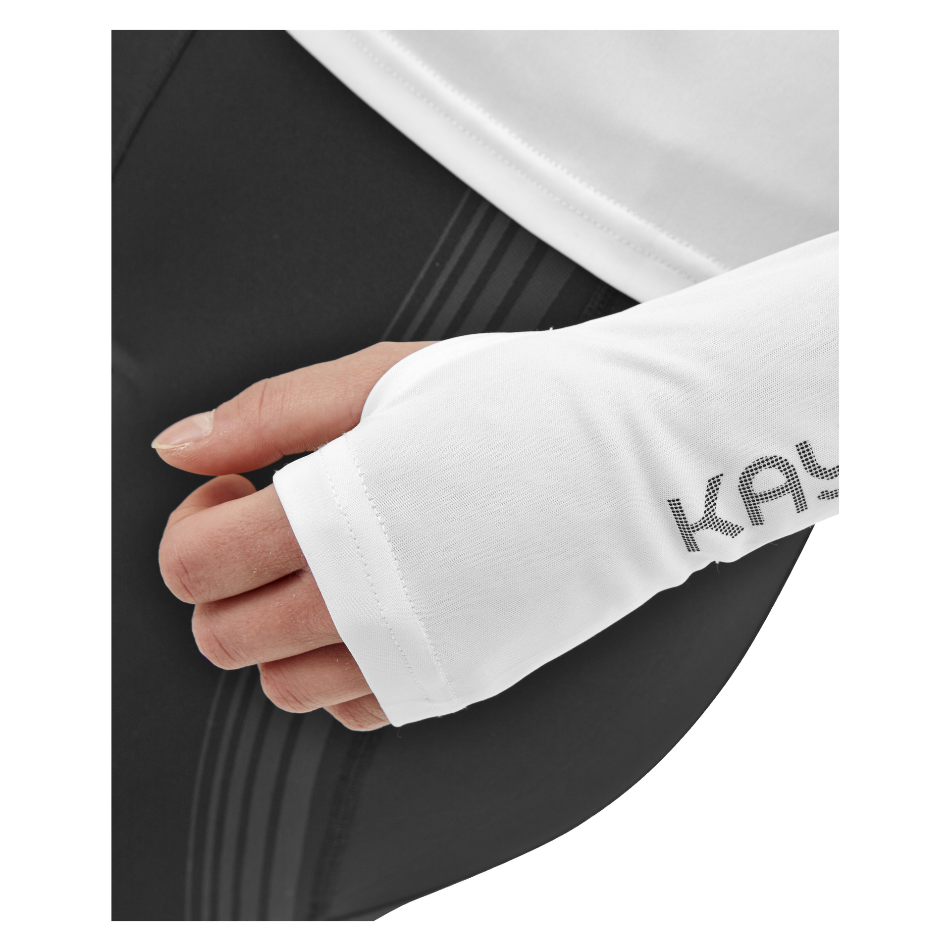 En närbild på en persons hand i en vit långärmad topp med tumhål, som visar den delvisa texten Kayoba. Personen är också klädd i Kayoba Tights damer Boston—svarta sportleggings med svaga vertikala ränder.