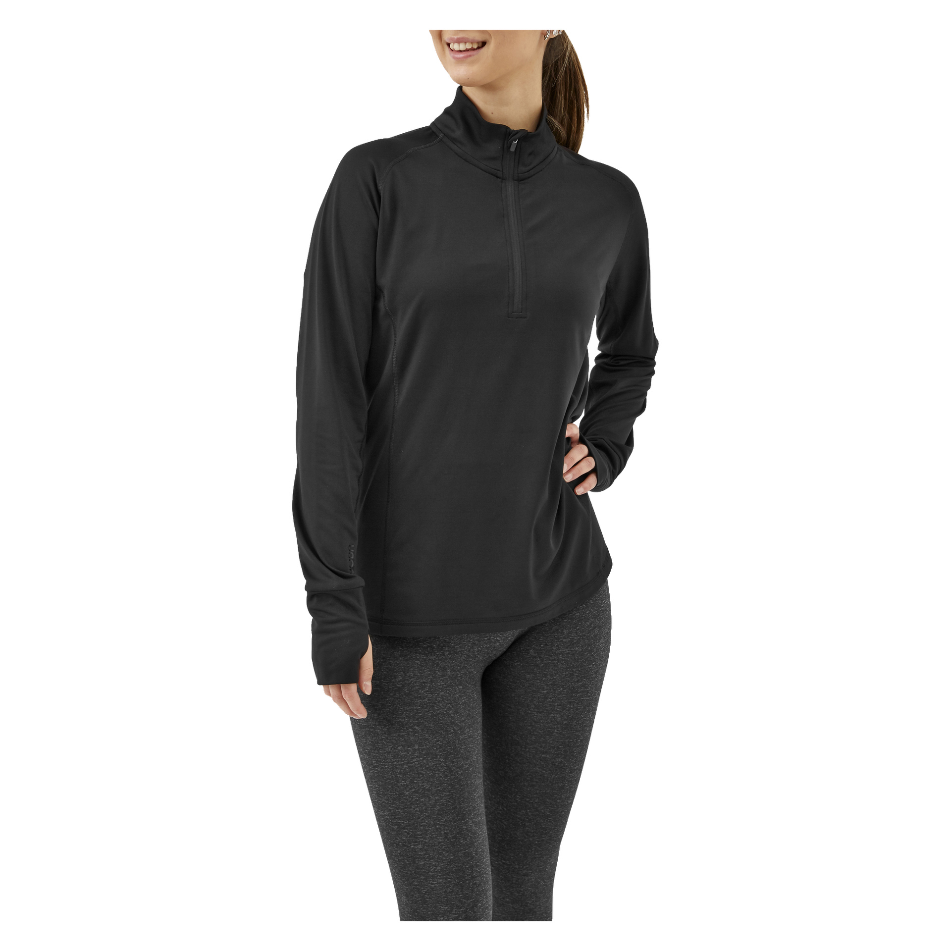 En kvinna som bär Kayoba Women's funktionella London-topp – en svart, långärmad tröja med kvartsdragkedja – tillsammans med mörkgrå leggings, står med ena handen på höften och ler.