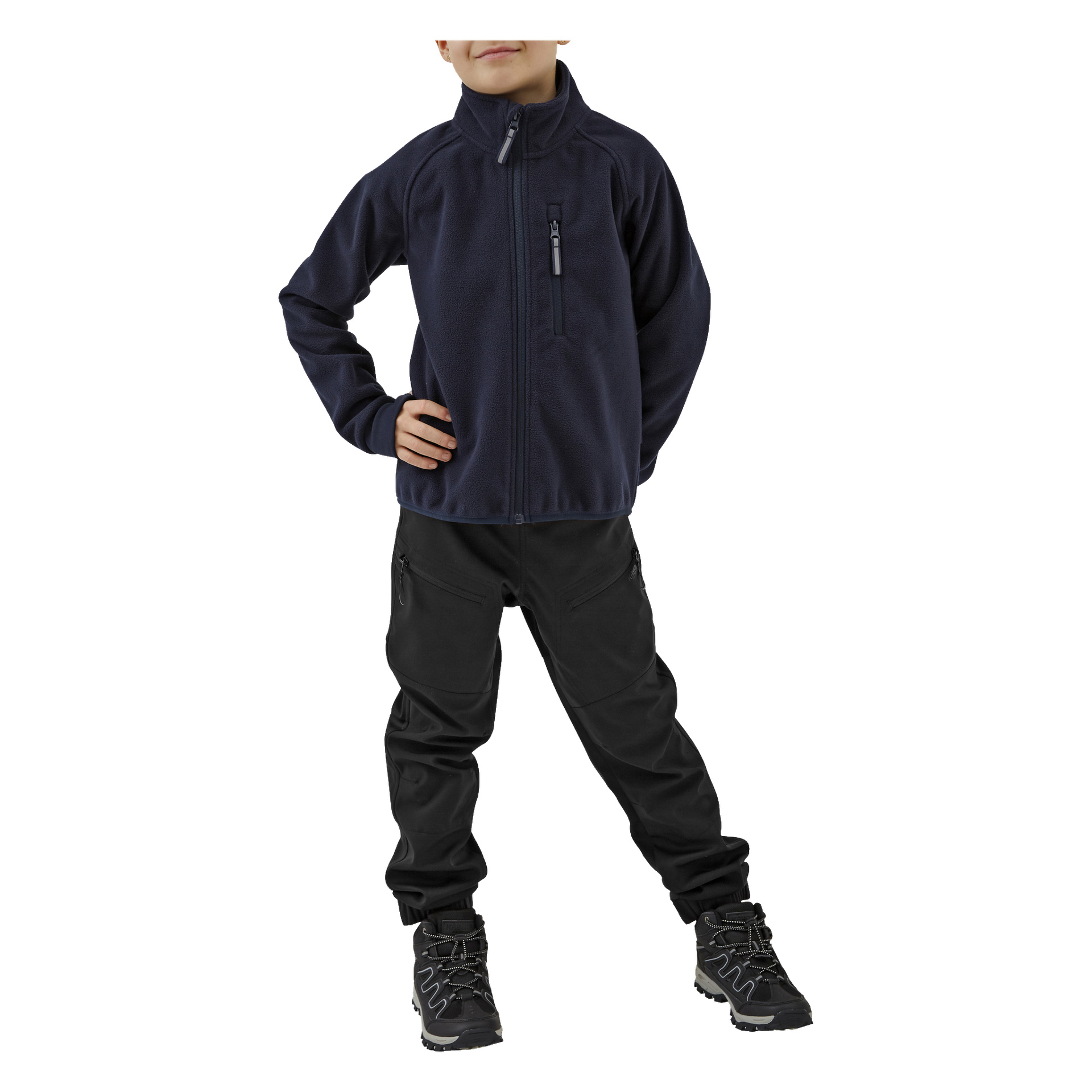 Ein Kind posiert mit einer Hand auf der Hüfte, gekleidet in Kayoba Outdoor-Kinderhosen, eine marineblaue Reißverschlussjacke und schwarze Wanderschuhe. Das Gesicht des Kindes ist teilweise außer Sichtweite.