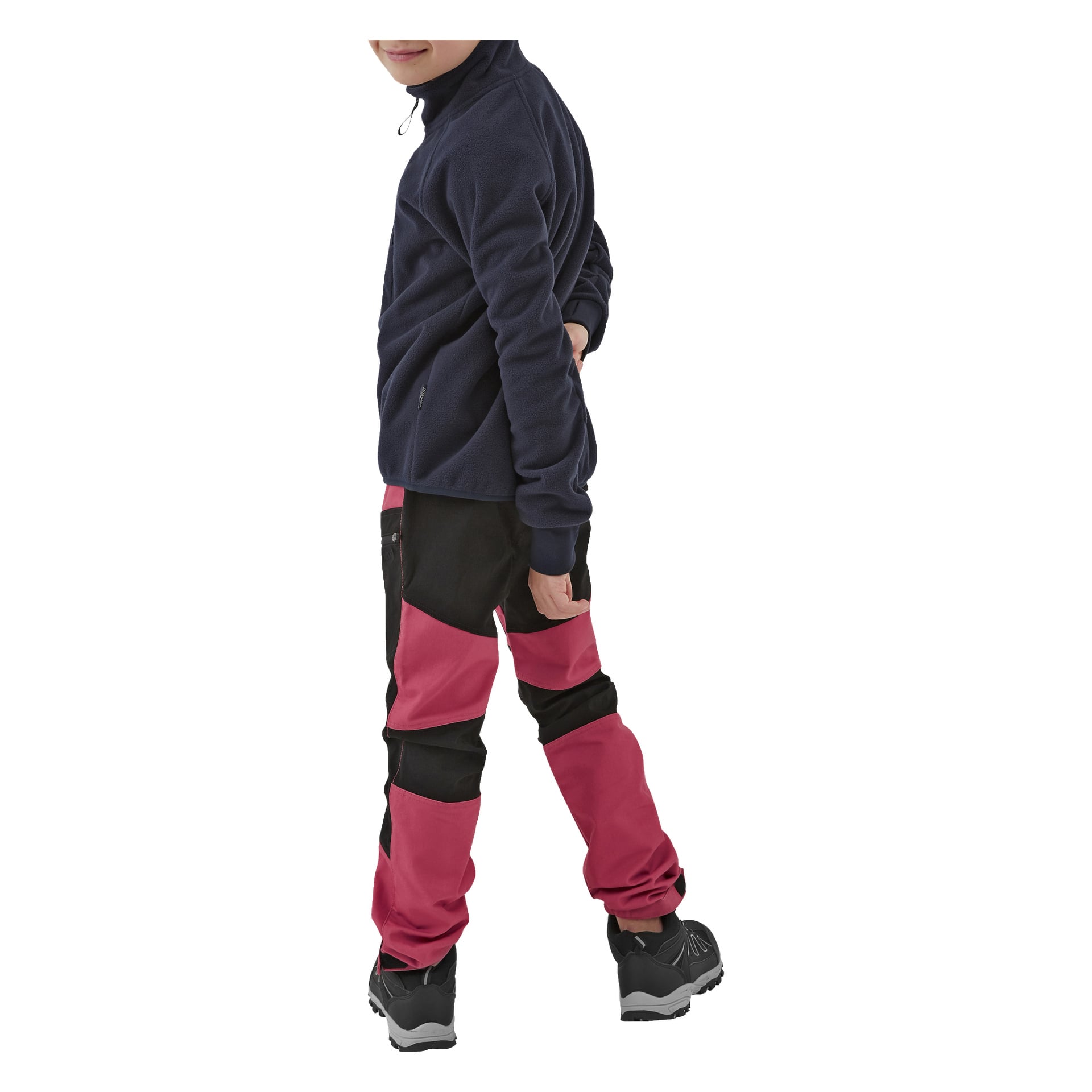 Ett barn klädt i svart och rött Kayoba Outdoor Barnbyxor Gävle, en marinblå fleecejacka och svarta sneakers står med ena handen bakom ryggen och kastar en blick över axeln.
