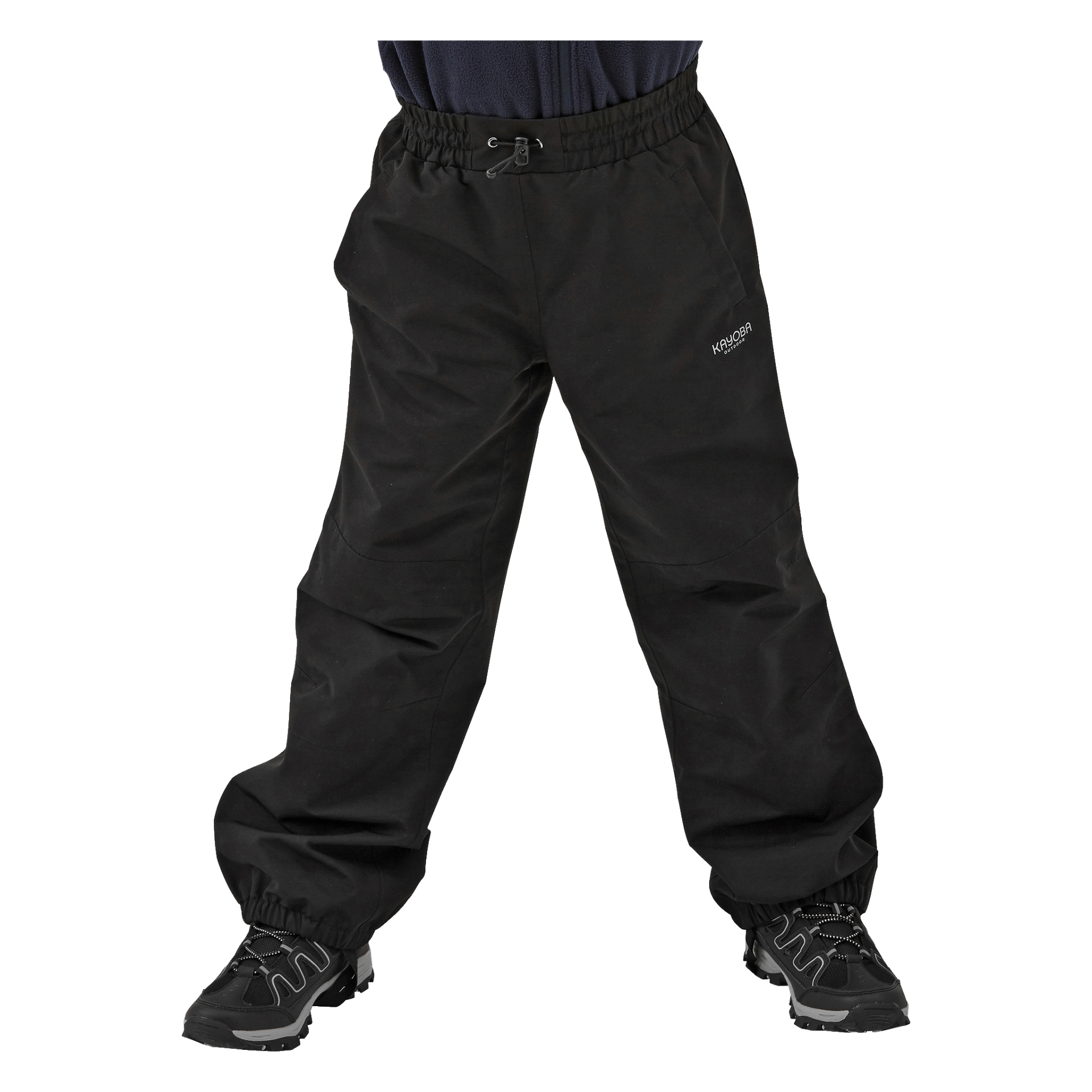 Ein Kind präsentiert locker sitzende schwarze Kayoba Outdoor Kinderhosen mit elastischen Manschetten und einem markanten elastischen Bund. Die Hosen zeigen ein kleines Logo am oberen linken Oberschenkel und werden mit schwarzen Turnschuhen kombiniert.