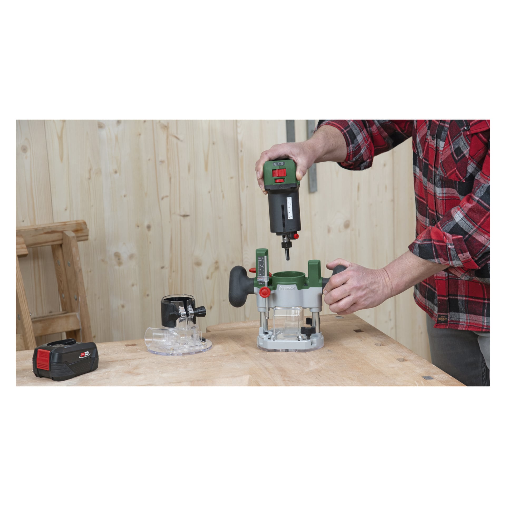 Mit einem roten karierten Hemd arbeitet man daran, den Bosch Power 4 All Combination Router AdvancedTrimRouter 18V-8 zusammenzubauen oder anzupassen, der an der Router Plunge Base befestigt ist und auf einer Holzwerkbank mit mehreren Aufsätzen und einer nahegelegenen Batterie steht. Die Szene spielt vor einer hellen, holzvertäfelten Wand im Hintergrund.