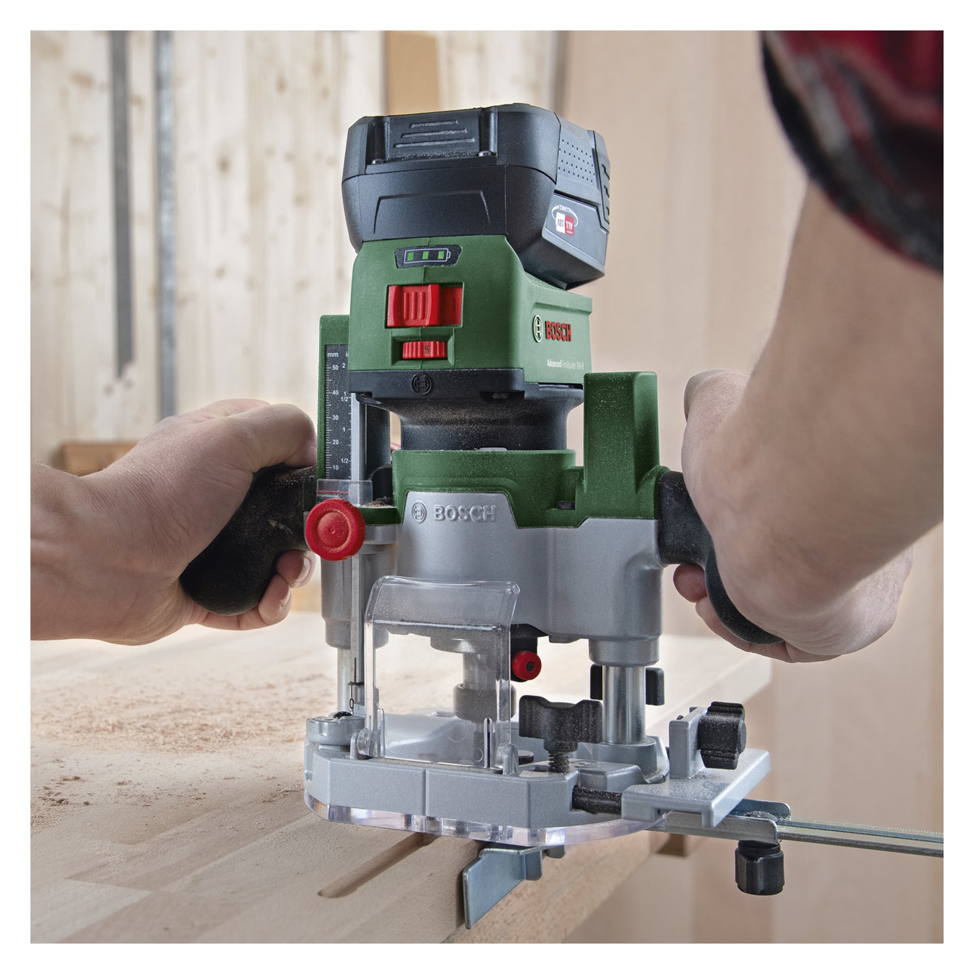 Man hält den Bosch Power 4 All Combination Router AdvancedTrimRouter 18V-8 fest mit der Fräs-Tauchbasis und schneidet damit eine Nut ins Holz. Holzspäne sind auf der Arbeitsfläche sichtbar, wenn das Werkzeug mit beiden Händen bedient wird.