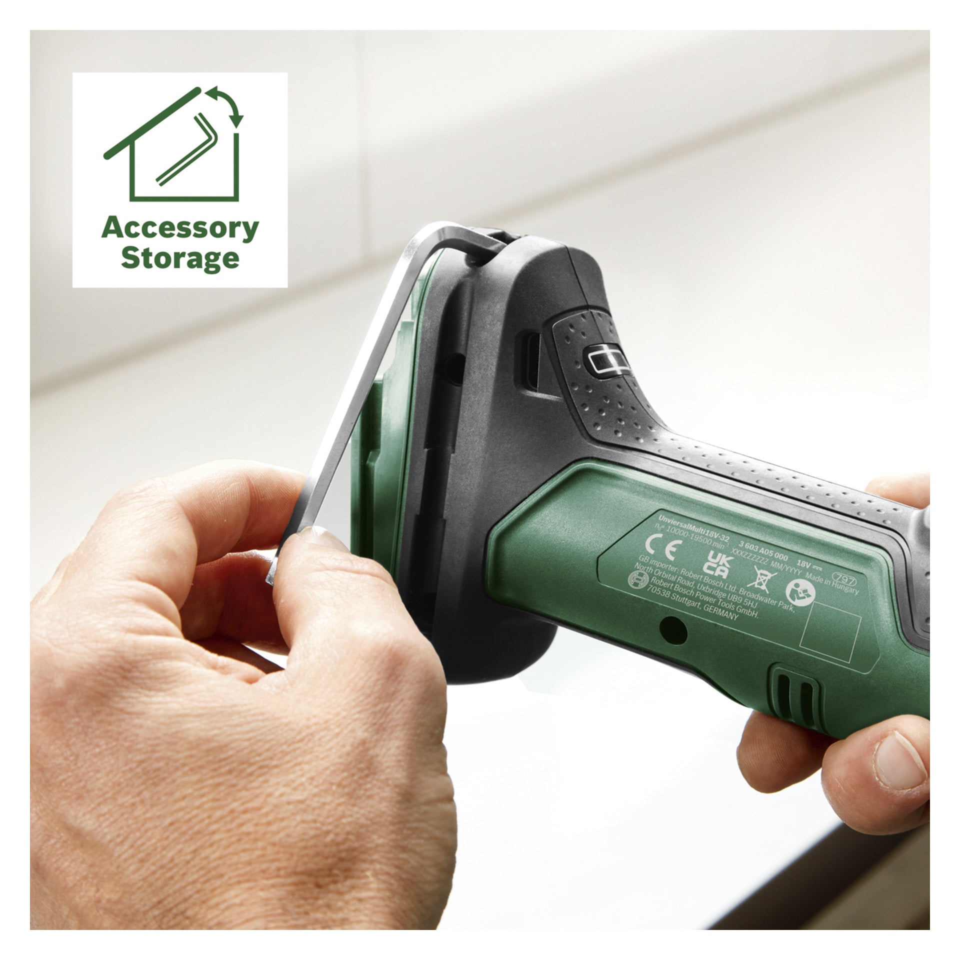 En person plasserer et metalltilbehør i oppbevaringsrommet på et grønt og svart Bosch Power 4 All UniversalMulti 18V-32 multifunksjonsverktøy. Øverst til venstre er det en Accessory Storage-etikett med et ikon.