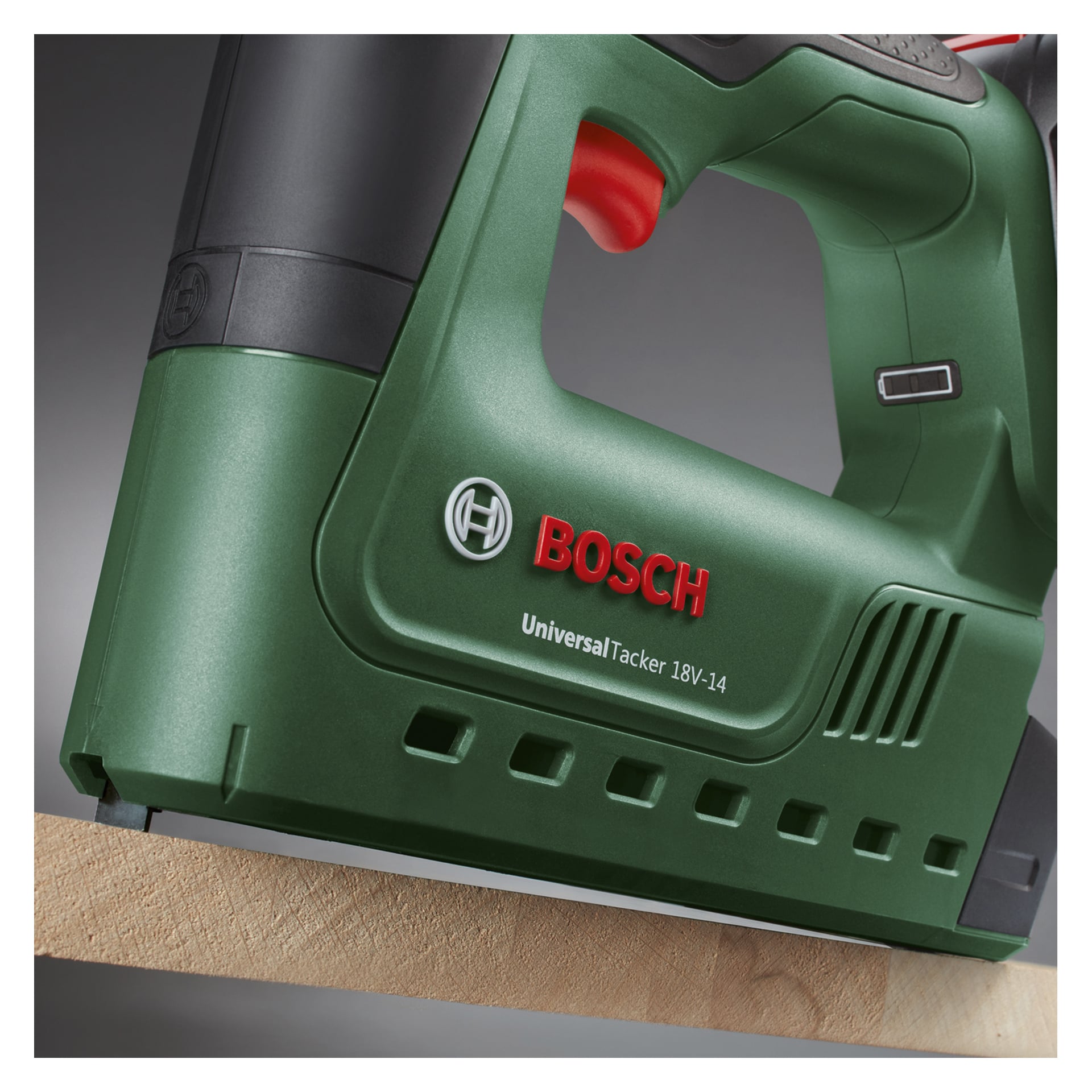 Detaillierte Ansicht eines grünen Bosch Power 4 All Cordless Hefters und einer Nagelpistole, Modell UniversalTacker 18V-14, die gegen eine Holzoberfläche gedrückt werden. Das Branding und die markanten Designmerkmale des Geräts sind deutlich sichtbar.