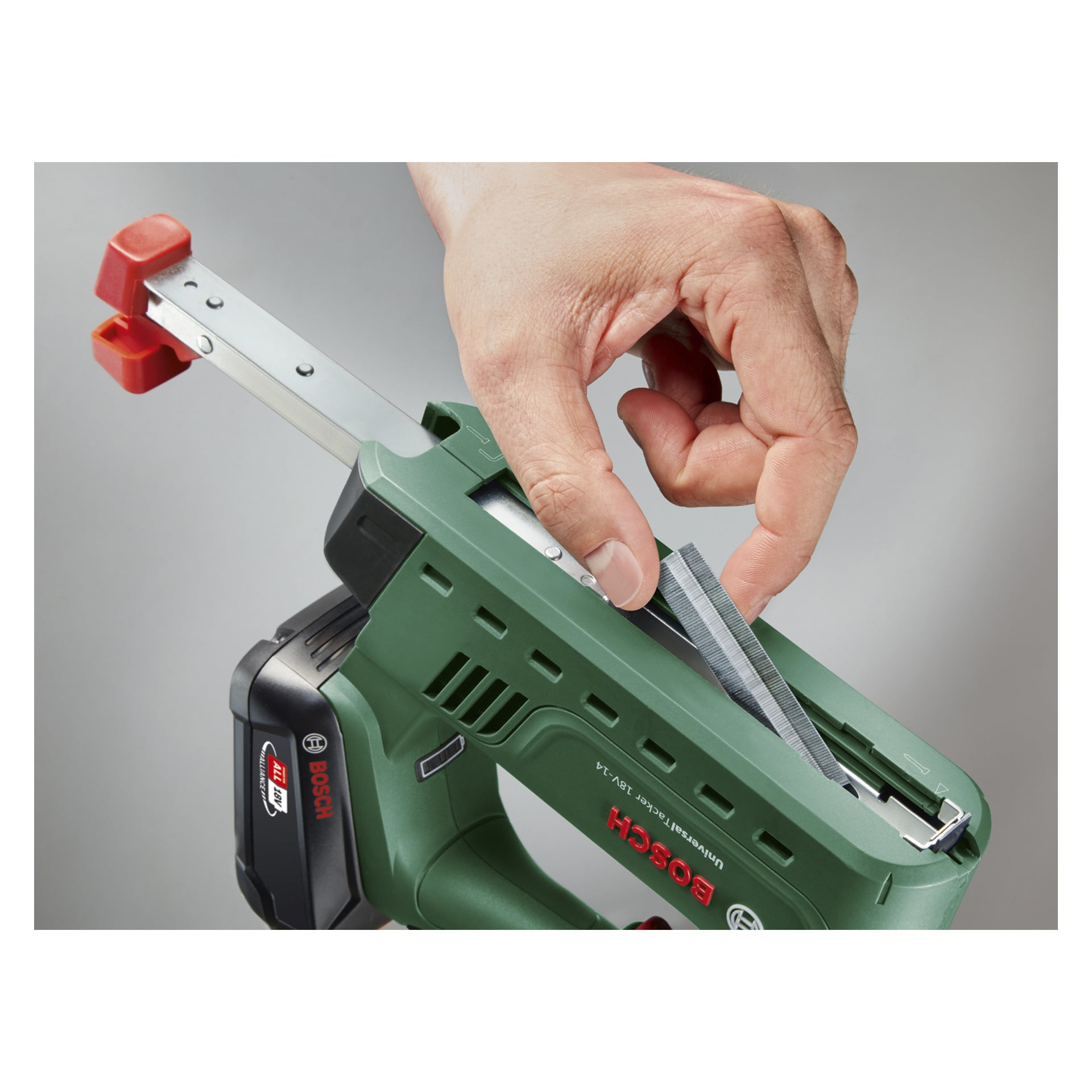 Eine Person steckt einen Klammerstreifen in einen grünen Bosch Power 4 All UniversalTacker 18V-14 batteriebetriebenen Tacker oder Nagelpistole mit grauem Hintergrund.