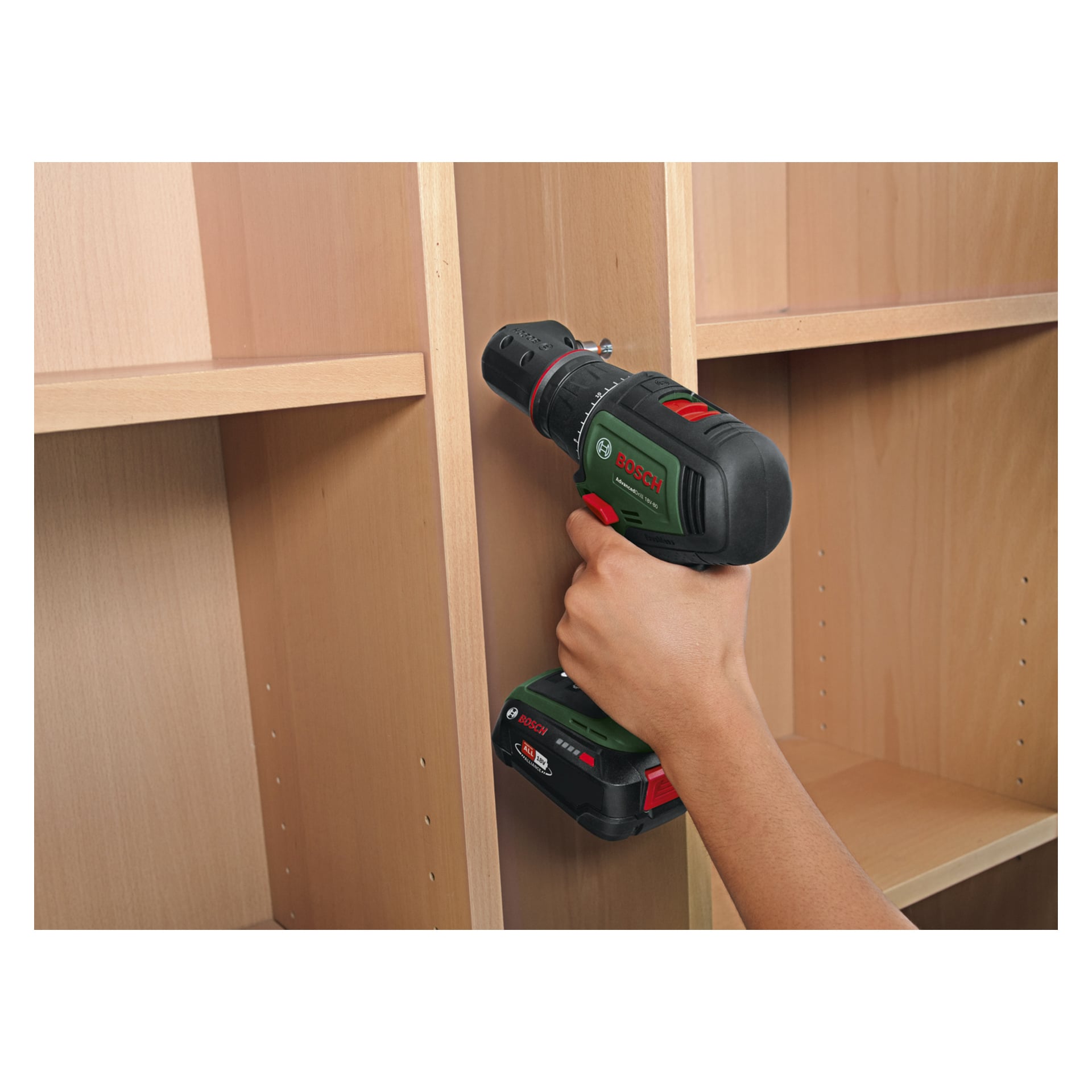 Käsi ohjaa Bosch Power 4 All Brushless AdvancedDrill 18V-80 -ruuvimeisseliä, joka työntää ruuvia pystysuoraan vaaleanruskeaan puupaneeliin hyllyllä. Pora on musta ja vihreä, jossa on tunnistettavat punaiset napit.