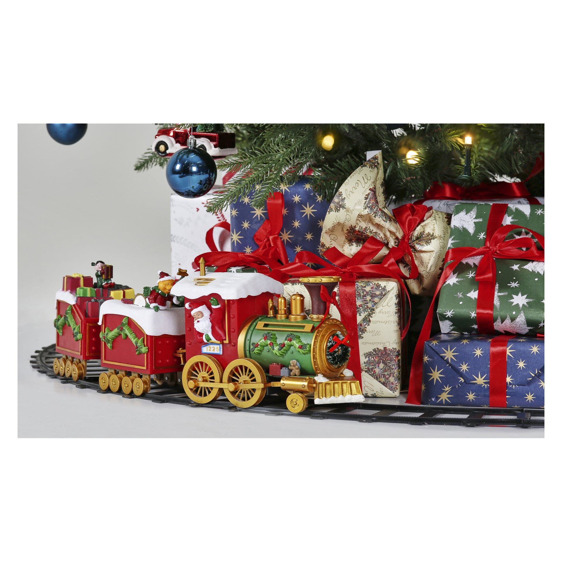 Ein EKVIP Weihnachtszug kreist unter dem Baum, umgeben von festlich verpackten Geschenken mit roten Bändern. Blaue Ornamente oben fangen das Licht ein und schaffen eine funkelnde Weihnachtsstimmung.