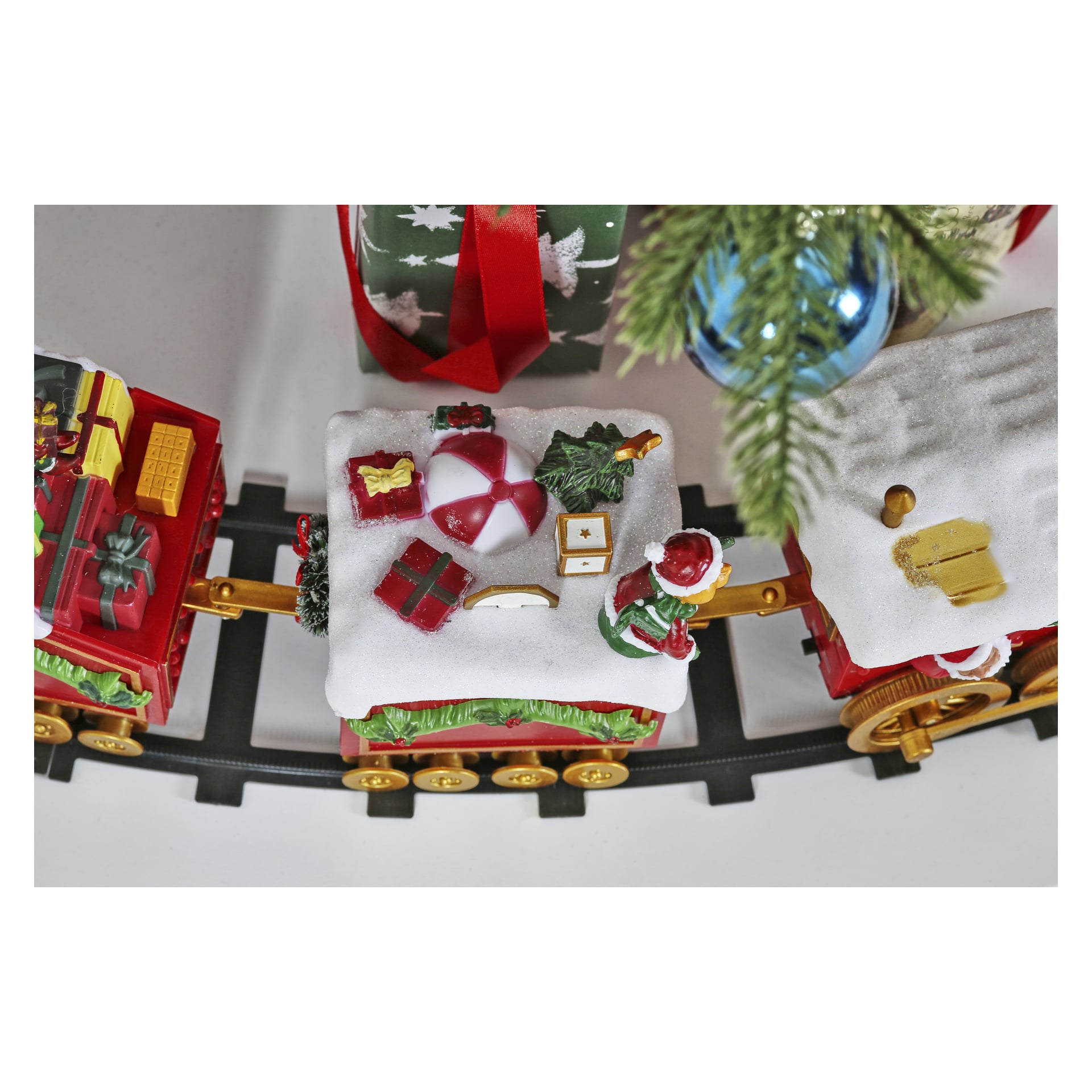 Ein festlicher EKVIP-Weihnachtszug steht auf den Gleisen, seine Wagen sind mit Kunstschnee, verpackten Geschenken, einem Strandball, einer Weihnachtsmannfigur und anderen Weihnachtsdekorationen geschmückt. In der Nähe liegen ein eingepacktes Geschenk und eine blaue Kugel.