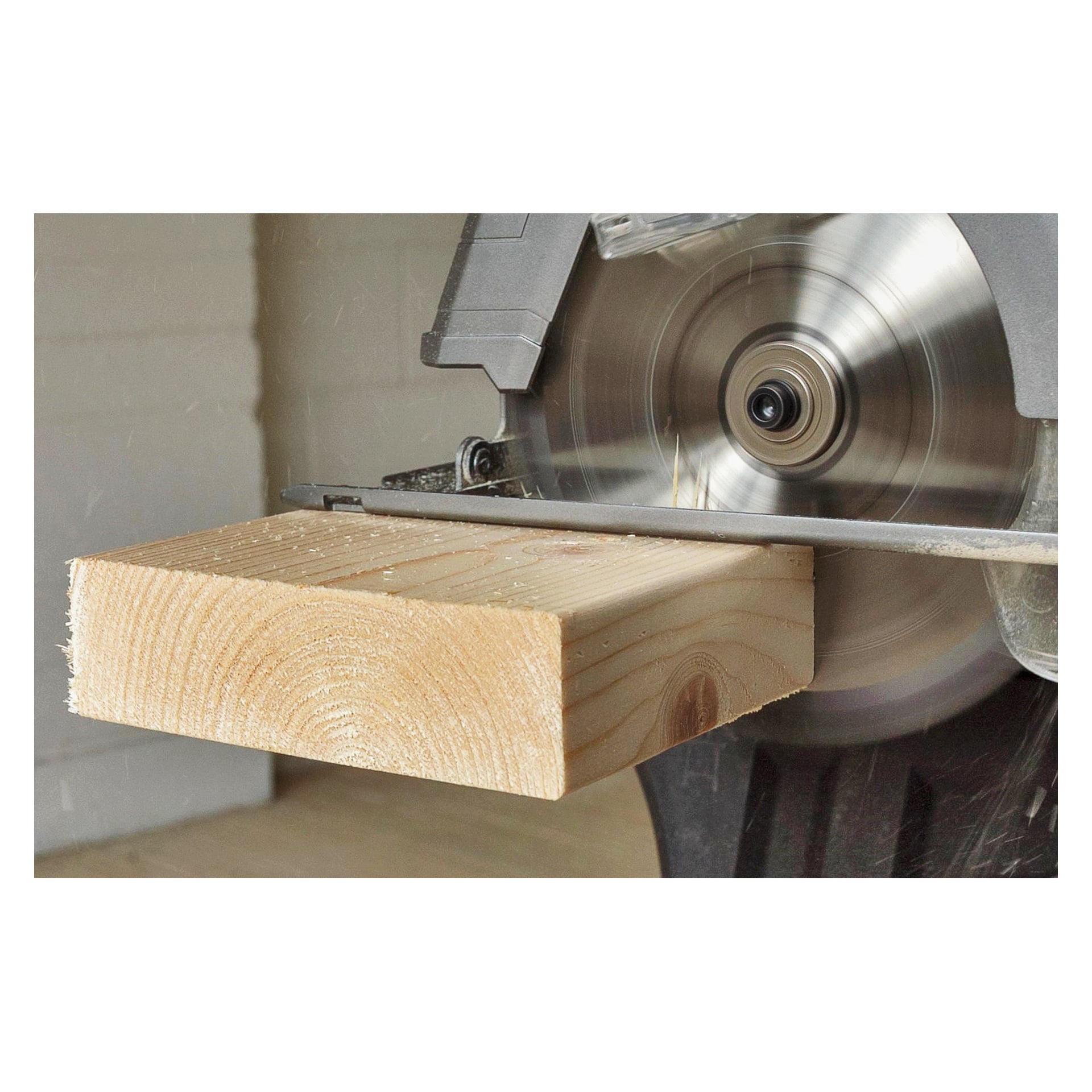 Die Ryobi One+ Kreissäge R18CS-140G schneidet aktiv durch ein blasses Holzbrett und schleudert Sägemehl durch die Luft, während ihre rotierende Klinge die detaillierten Ringe und Maserung des Holzes freilegt.