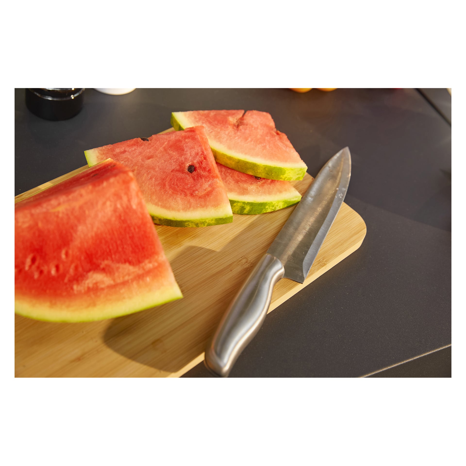Wassermelonenscheiben liegen auf einem Holzschneidebrett neben einem großen Küchenmesser aus dem Menuett Knives + Messerblock 5-teiliges Set. Helles Licht hebt das Setup hervor, mit einem sanft verschwommenen Hintergrund.