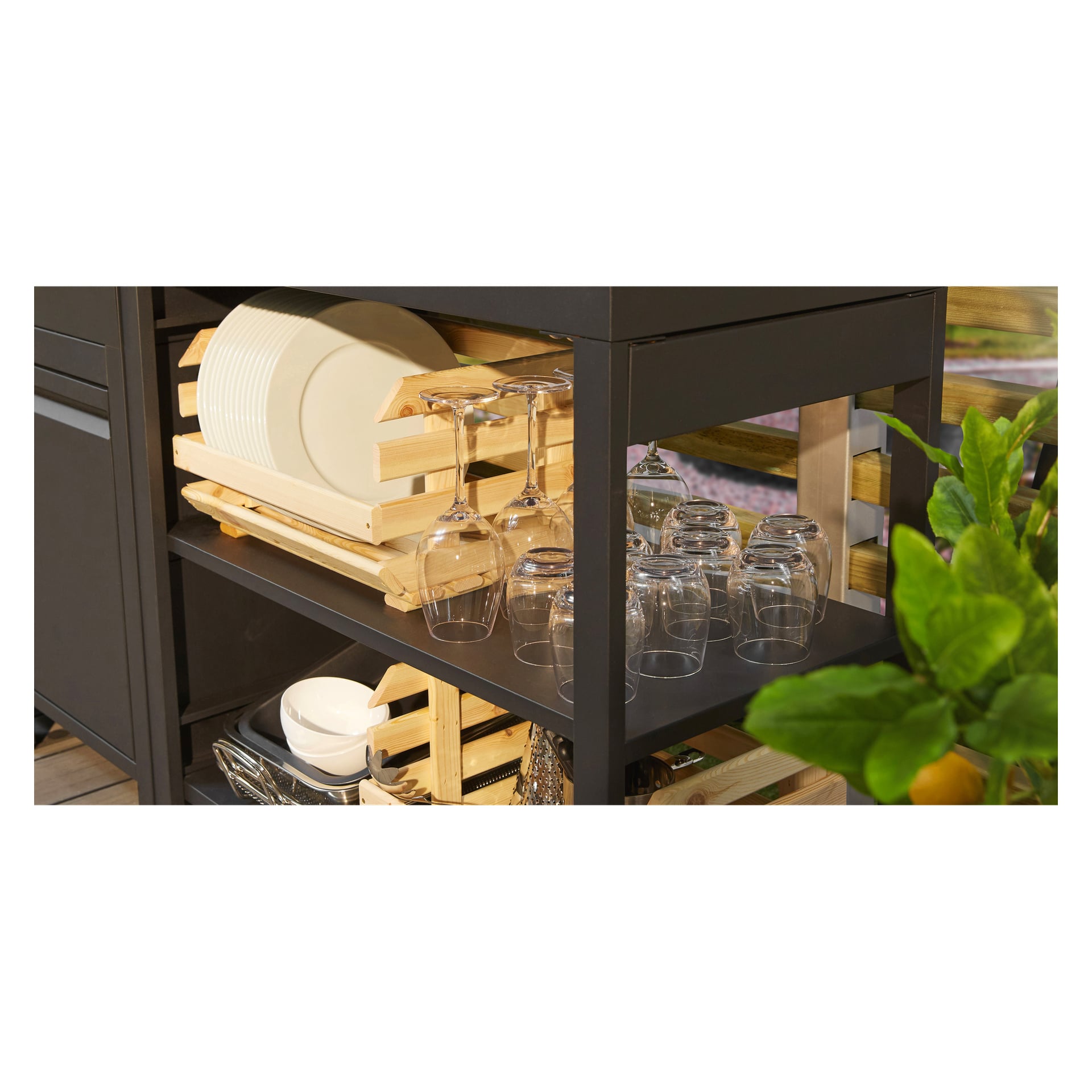 Auf einem schwarzen Metallregal ordnet ein hölzernes Geschirrregal Teller und Weingläser. Oben und unten zeigen weitere Regale weitere Menuett Trinkglas 2 Packs und verschiedene Schalen. Eine grüne Pflanze bringt Farbe im Vordergrund.