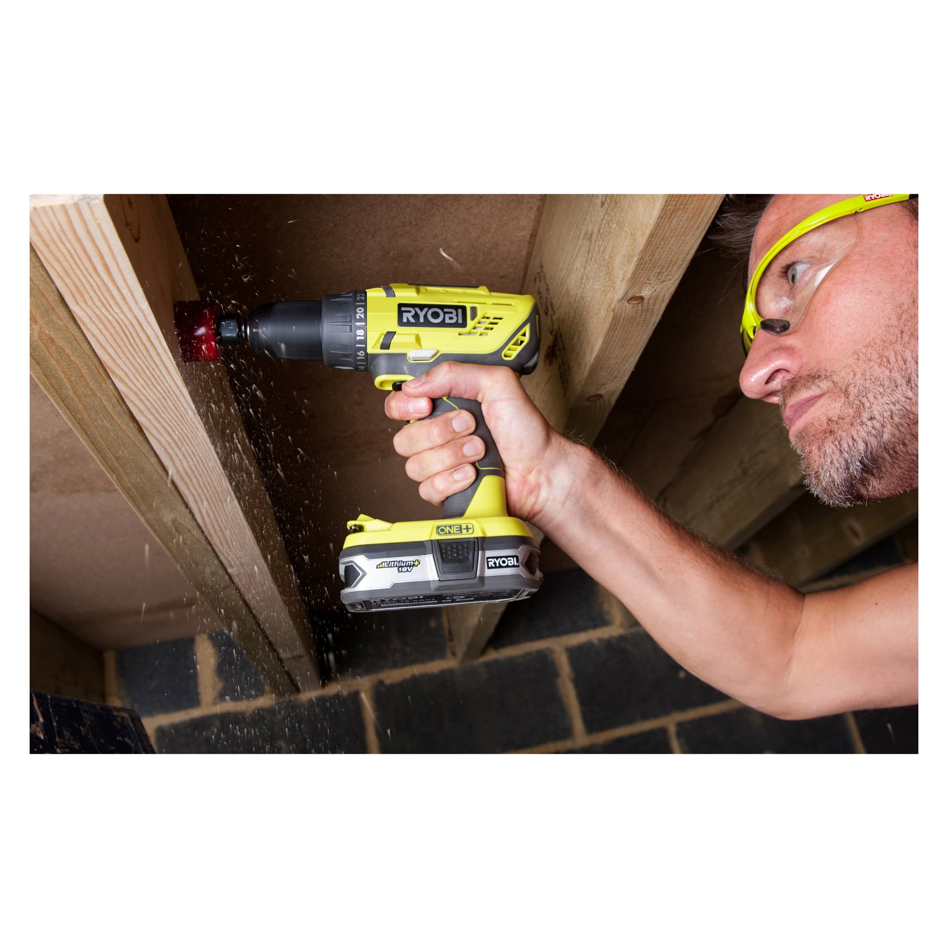 En person med skyddsglasögon borrar i en träbalk med en Ryobi One+ Screwdriver R18DD32-0 sladdfri borrmaskin, vilket ger synliga träspån från arbetet.