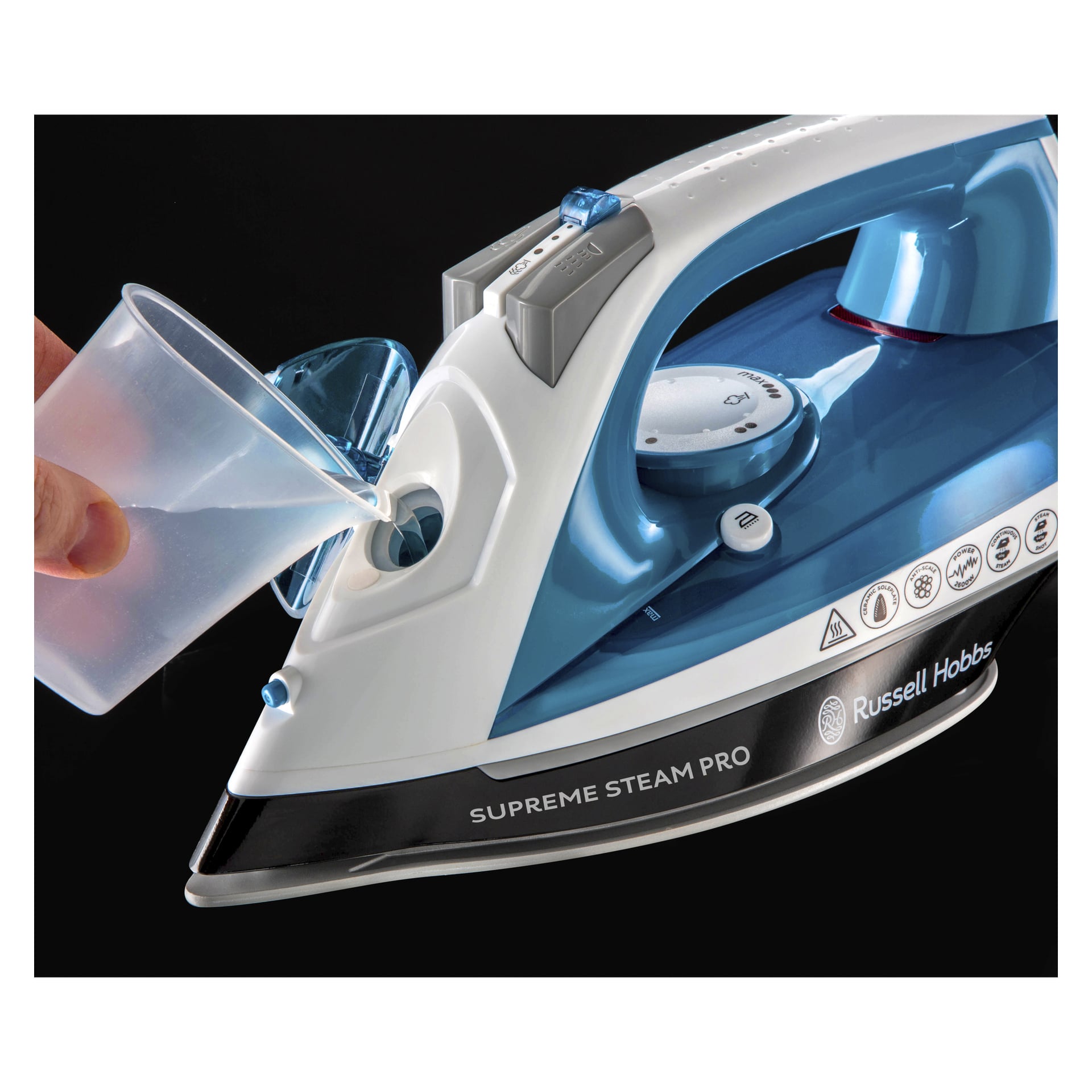 Wasser wird aus einem Plastikmessbecher in den Wassertank eines blau-weißen Russell Hobbs Iron Supreme Steam Pro gegossen, der vor schwarzem Hintergrund gezeigt wird.