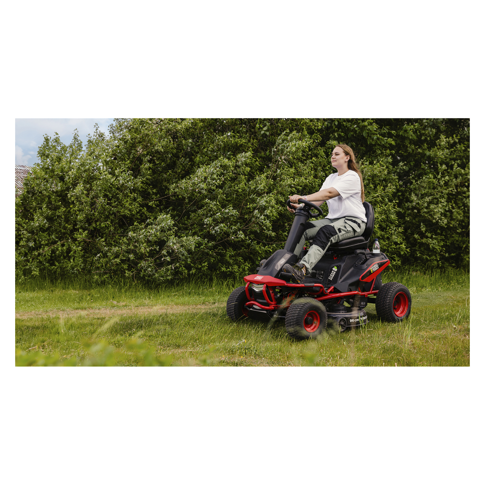 Jemand, der ein weißes Hemd und grüne Hosen trägt, bedient einen rot-schwarzen, batteriebetriebenen Meec Tools Rasenmäher und bewegt sich durch eine von Büschen und Bäumen umgebene Grasfläche.