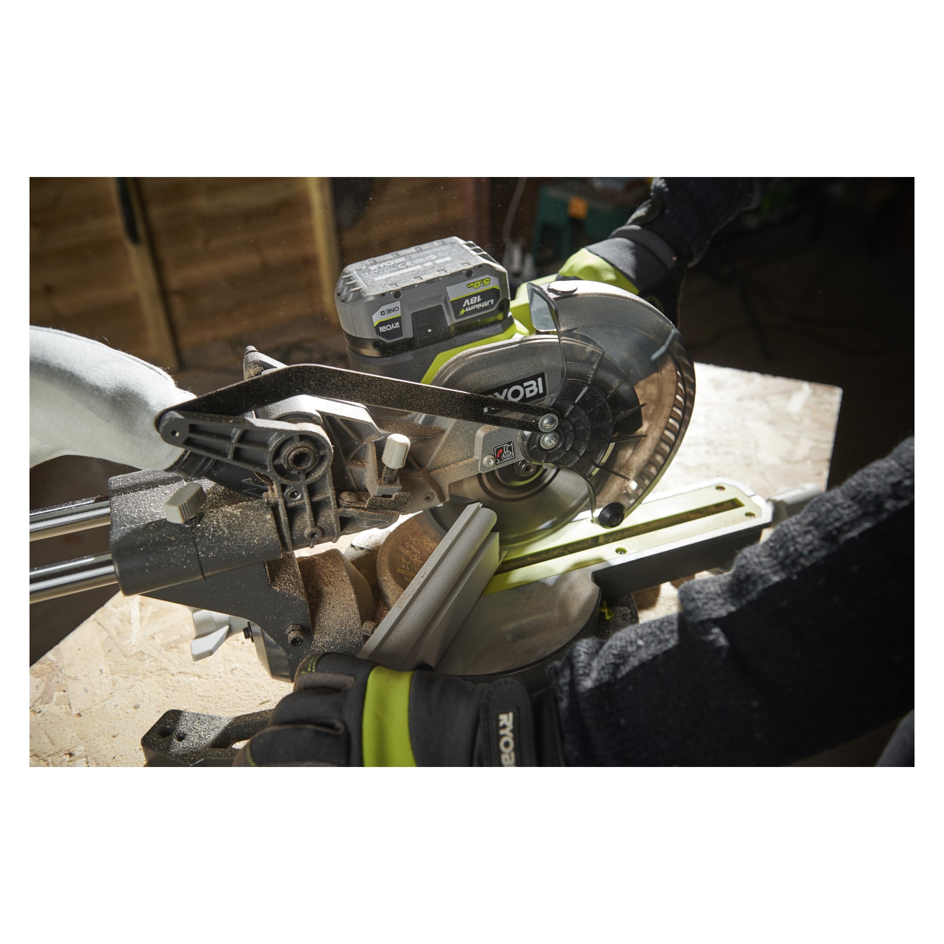 En person som bär handskar använder Ryobi One+ RMS18190-0 batteridriven geringssåg, där trälister på en arbetsbänk samlas runt sågspån.