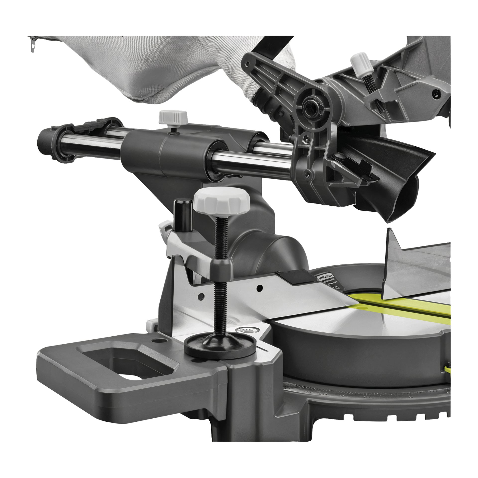 Detaljerad vy av Ryobi One+ Batteridrivna mitresåg RMS18190-0 visar dess roterande blad, vinkeljusteringsrattar och ett slitstarkt metallstaket. En dammuppsamlingspåse sitter upptill, och sågen visar upp ett grått och svart färgschema med gröna accenter.