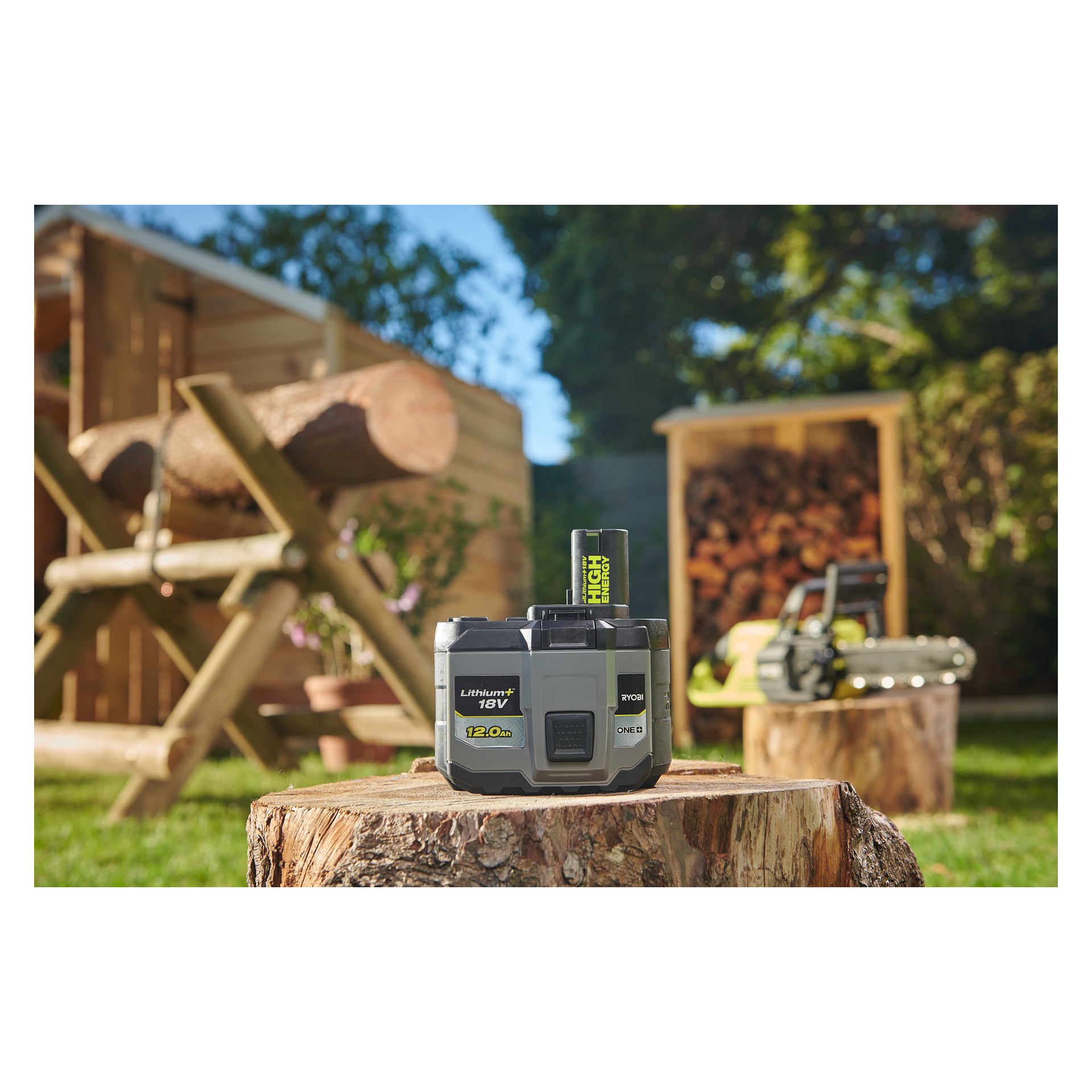 En "Ryobi One+ Battery High Energy RB18120T" står på en trestubbe i en solrik hage, med motorsag, huggd ved, en tømmerbenk og et treskur i bakgrunnen.