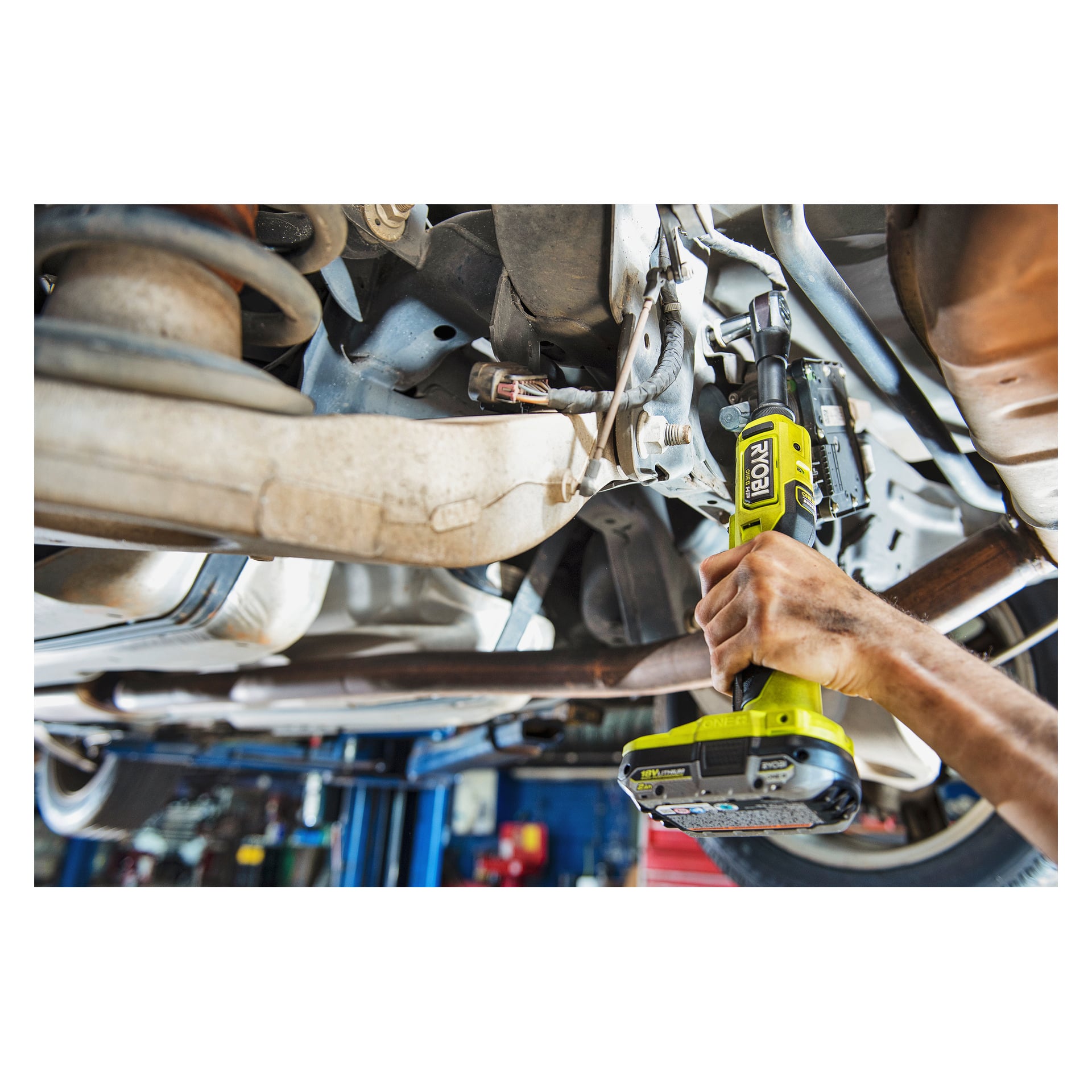 Mechanik obsługuje limonkowo-zieloną rączkę grzechotki Ryobi One+ HP zasilaną bateriami (model RRW1838X-0), aby zabezpieczyć śrubę pod podwoziem samochodu podniesionym na podnośniku warsztatowym.