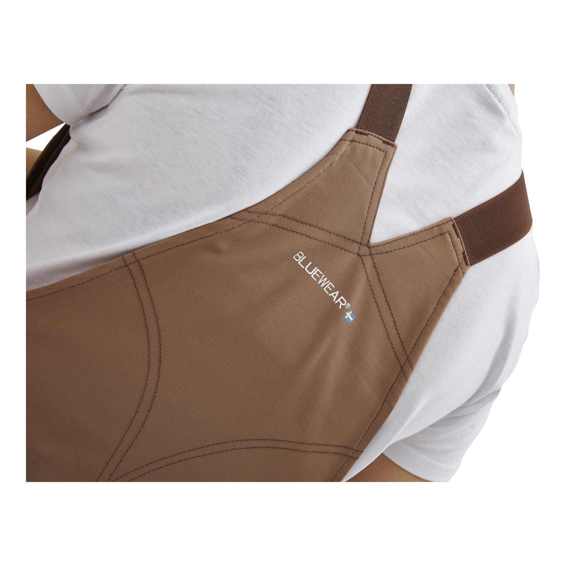 Et nærbilde av noen kledd i damekjeledressen Jill by Bluewear, som viser et brunt forkle med «BLUEWEAR» og et lite blått og hvitt flagg-logo.