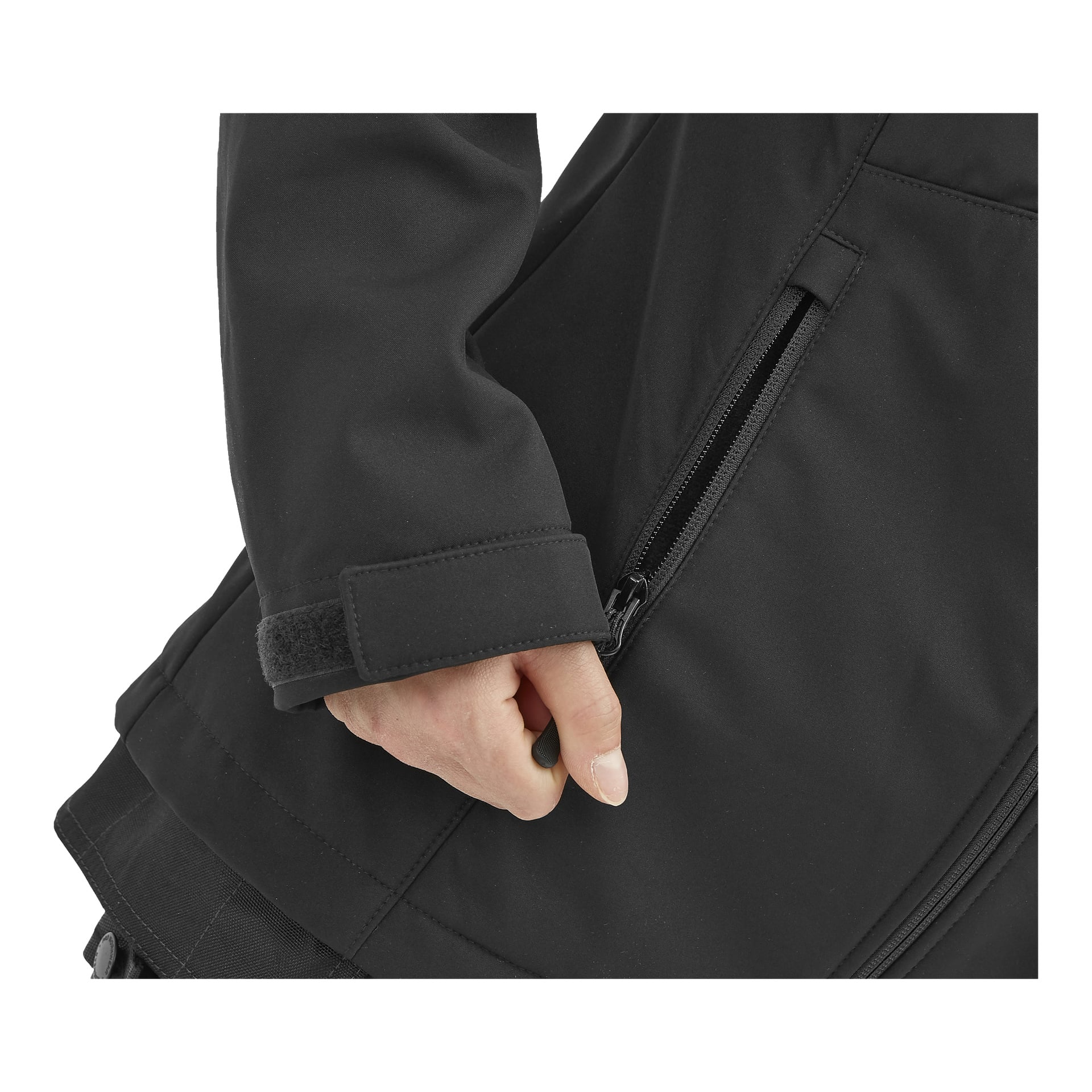 Henkilö kiinnittää tarranauhan mustaan Bluewear Jenny -naisten kevyesti pehmustettuun softshell-takkiin. Painopiste on hihassa, jossa on vetoketjullinen tasku, ja henkilön kädessä, taustalla on yksinkertainen, huomaamaton tausta.