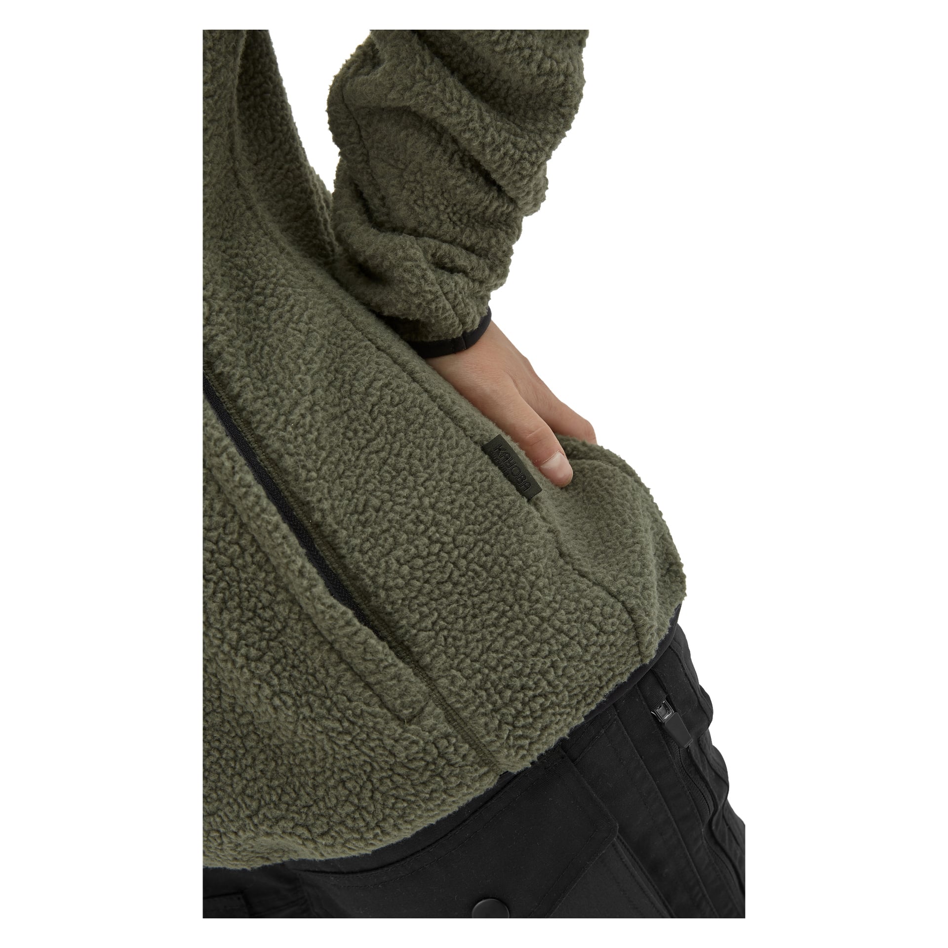 Eine Nahaufnahme zeigt eine Person, die eine olivgrüne Kayoba Outdoor Woman's Fleecejacke Ljusdal und schwarze Hose trägt, wobei eine Hand lässig in die Jackentasche steckt. Das Fleece hat ein weiches, strukturiertes Aussehen.