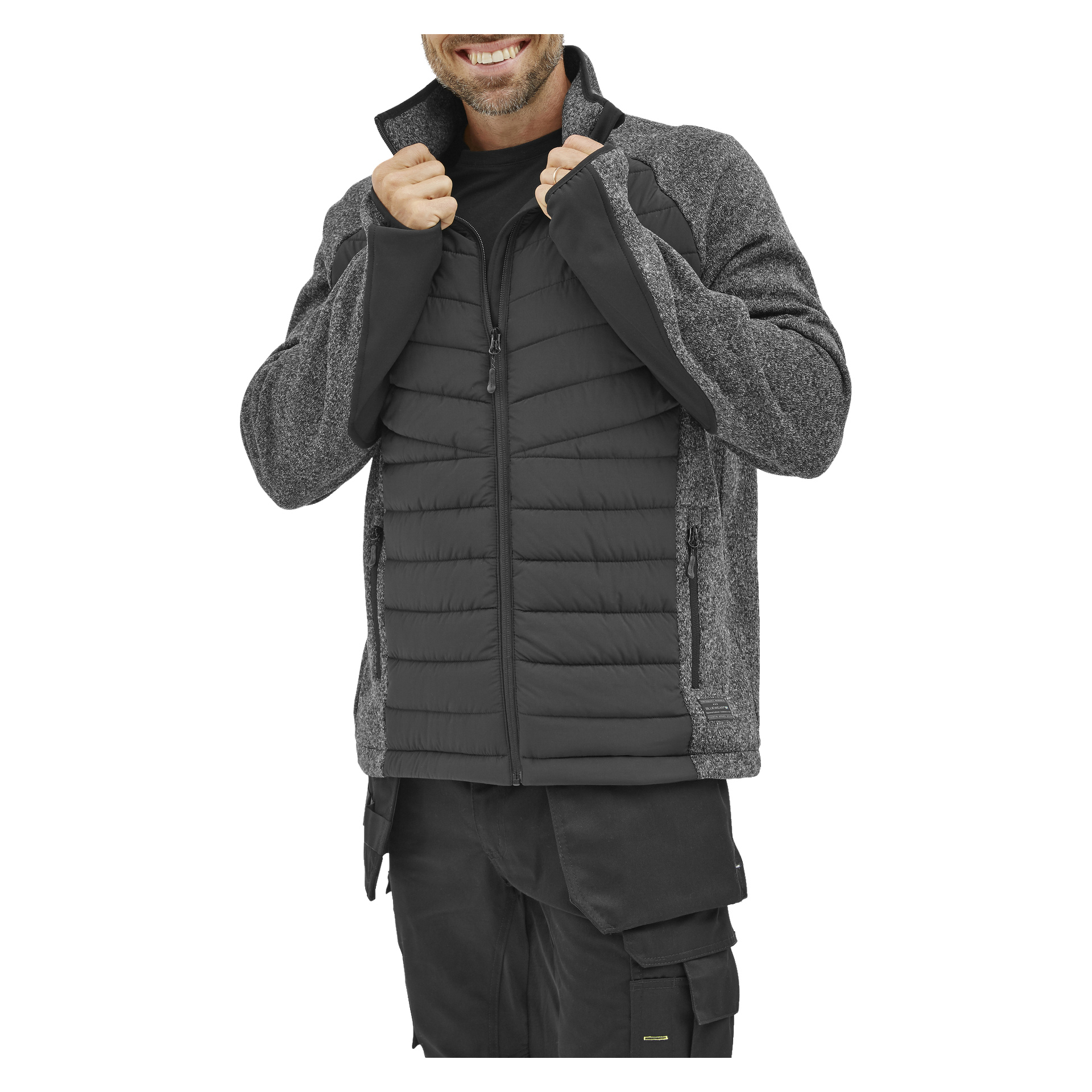 Osoba w hybrydowej kurtce Hilmer Bluewear Men's, z pikowanym przodem i ciemnymi rękawami, uśmiecha się i podnosi kołnierz. Jej twarz jest częściowo widoczna, a także ma na sobie czarne spodnie cargo.