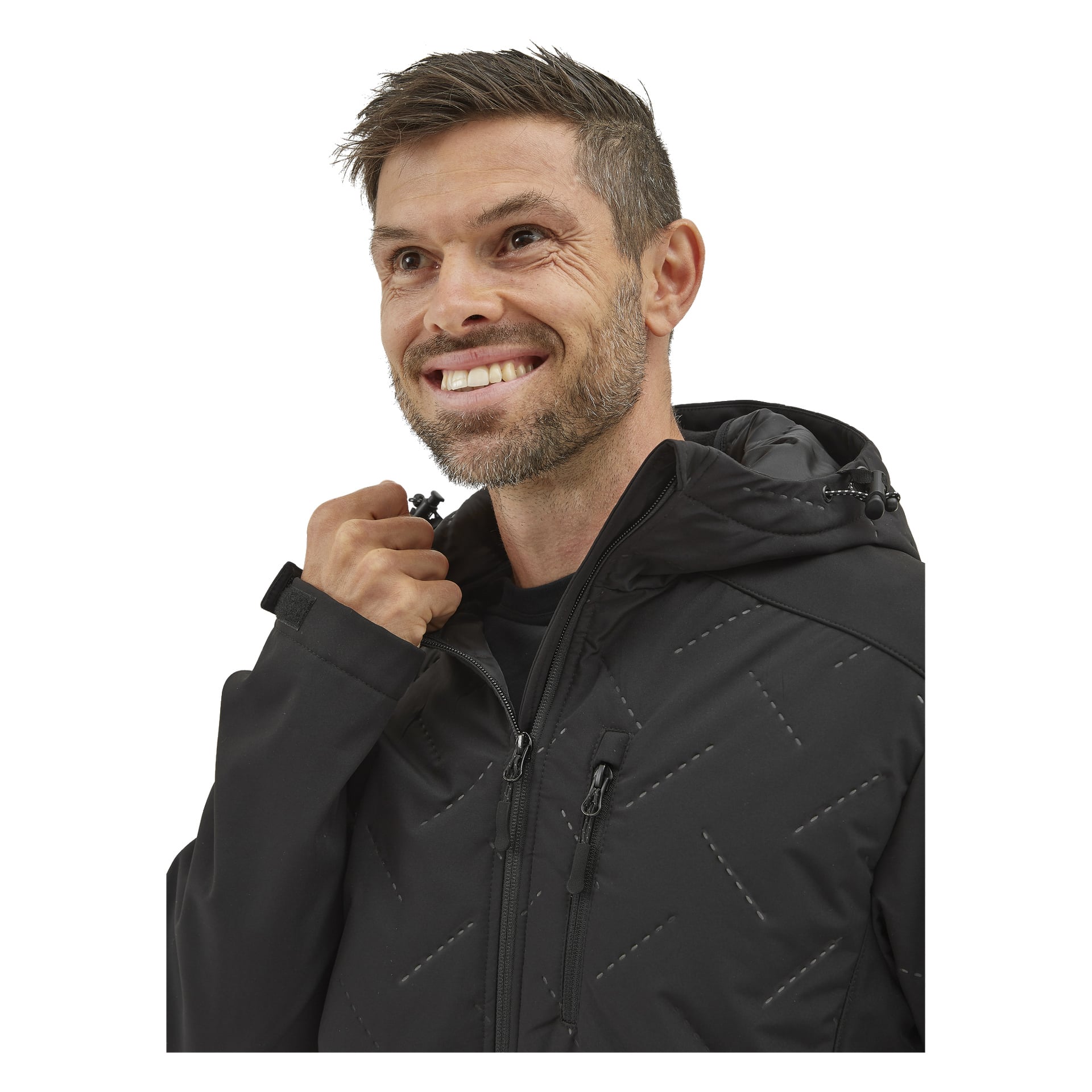 En man med kort hår och skägg ler när han drar upp Bluewear Lättvadderade herrsoftshell-jackan Jerry i svart.
