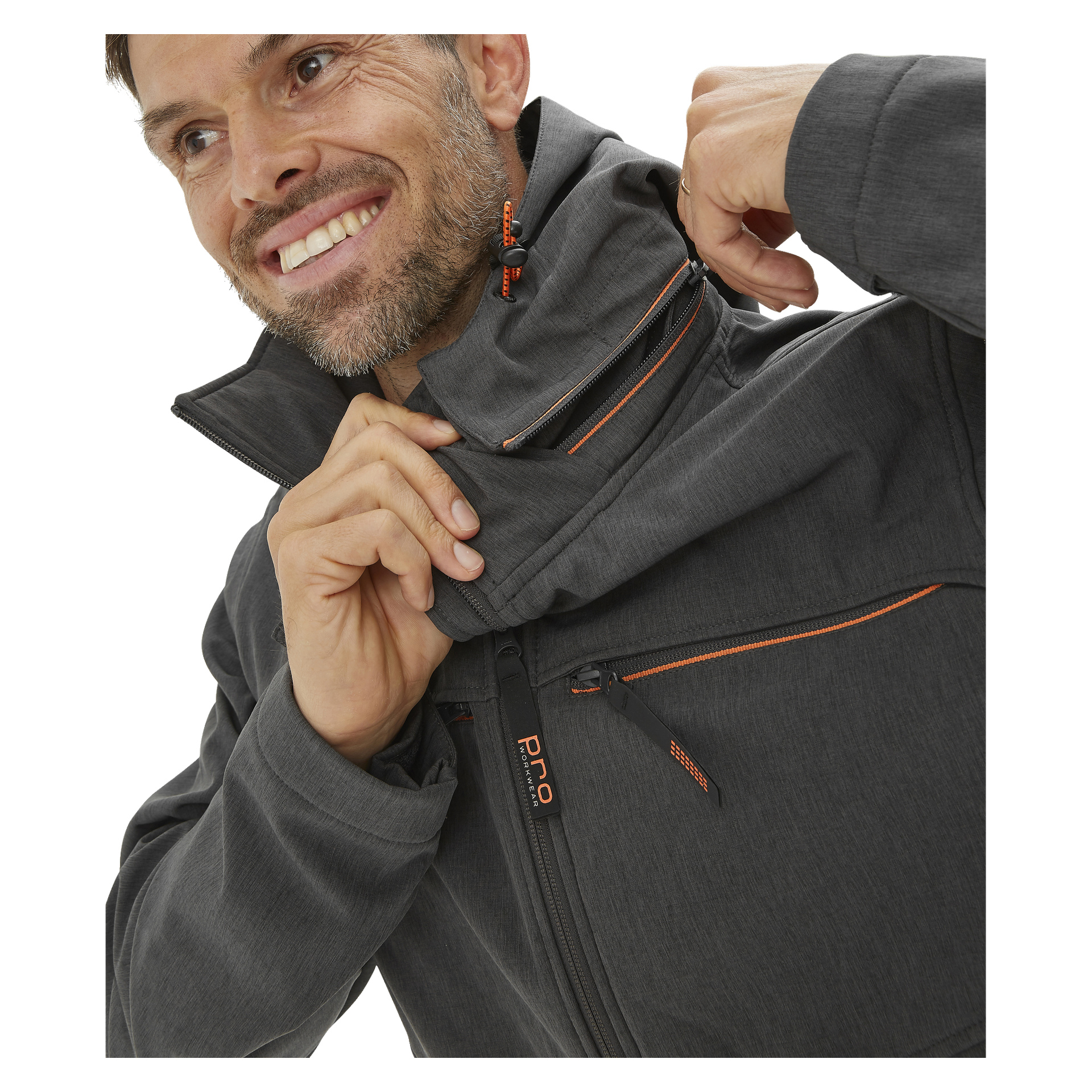 En man i en grå Bluewear Pro Workwear Pontus softshelljacka med orange detaljer justerar den höga kragen och ler, vilket drar uppmärksamheten till den dragkedjasförsedda bröstfickan och den precisa sömmen.