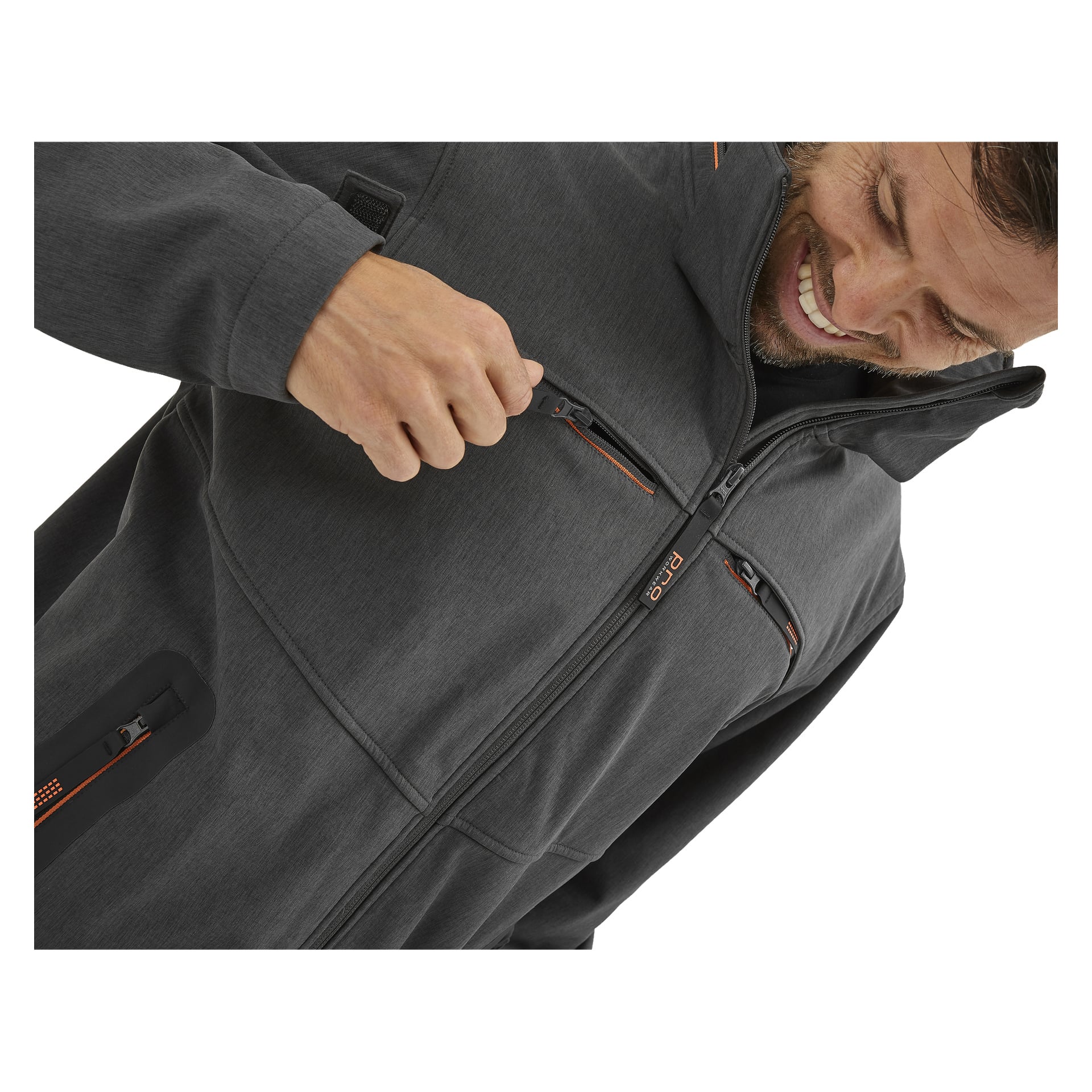 En man ler och tittar ner när han drar ner dragkedjan på bröstfickan på sin Bluewear Pro Workwear Pontus softshell-jacka, som har flera fickor med dragkedjeförsedda detaljer och orangea detaljer.