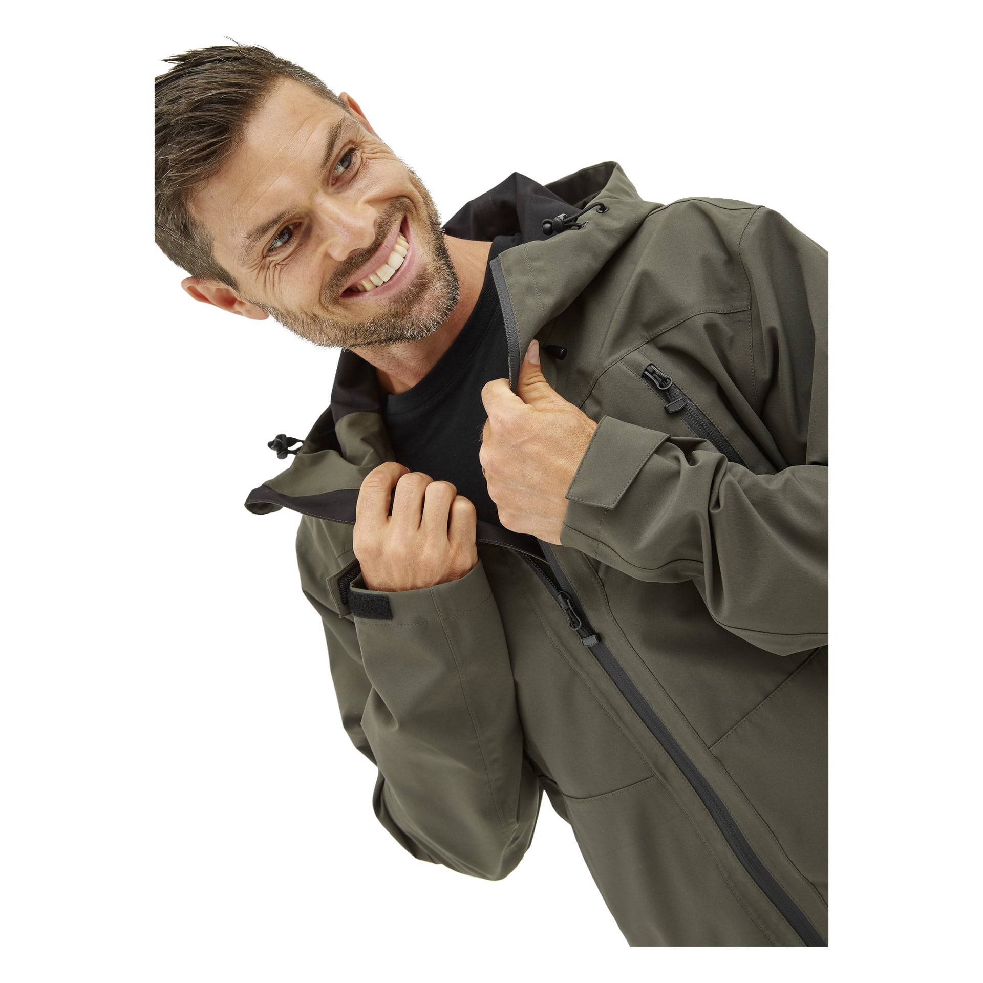 En man med kort hår ler och tittar åt sidan medan han drar upp en grön Kayoba Outdoor Men's Helag-shelljacka över en svart skjorta.