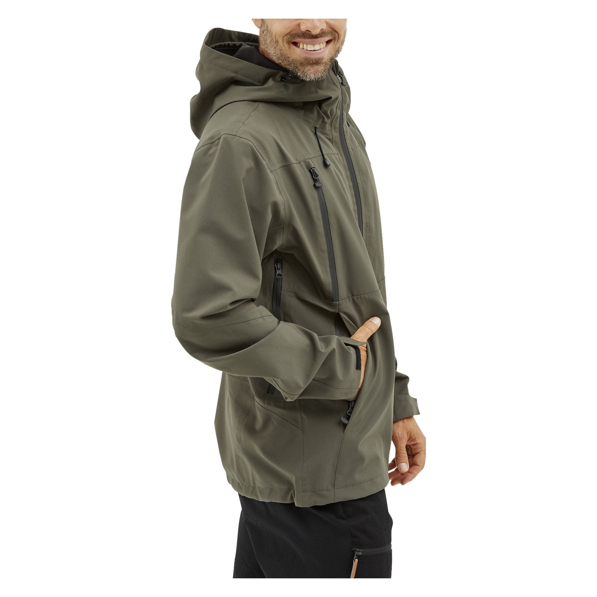 En man poserar i vinkel med ett leende, klädd i olivgrön Kayoba Outdoor Men's shelljacka Helag och svarta byxor. Jackan har flera fickor med dragkedja och tumhål på ärmarna.