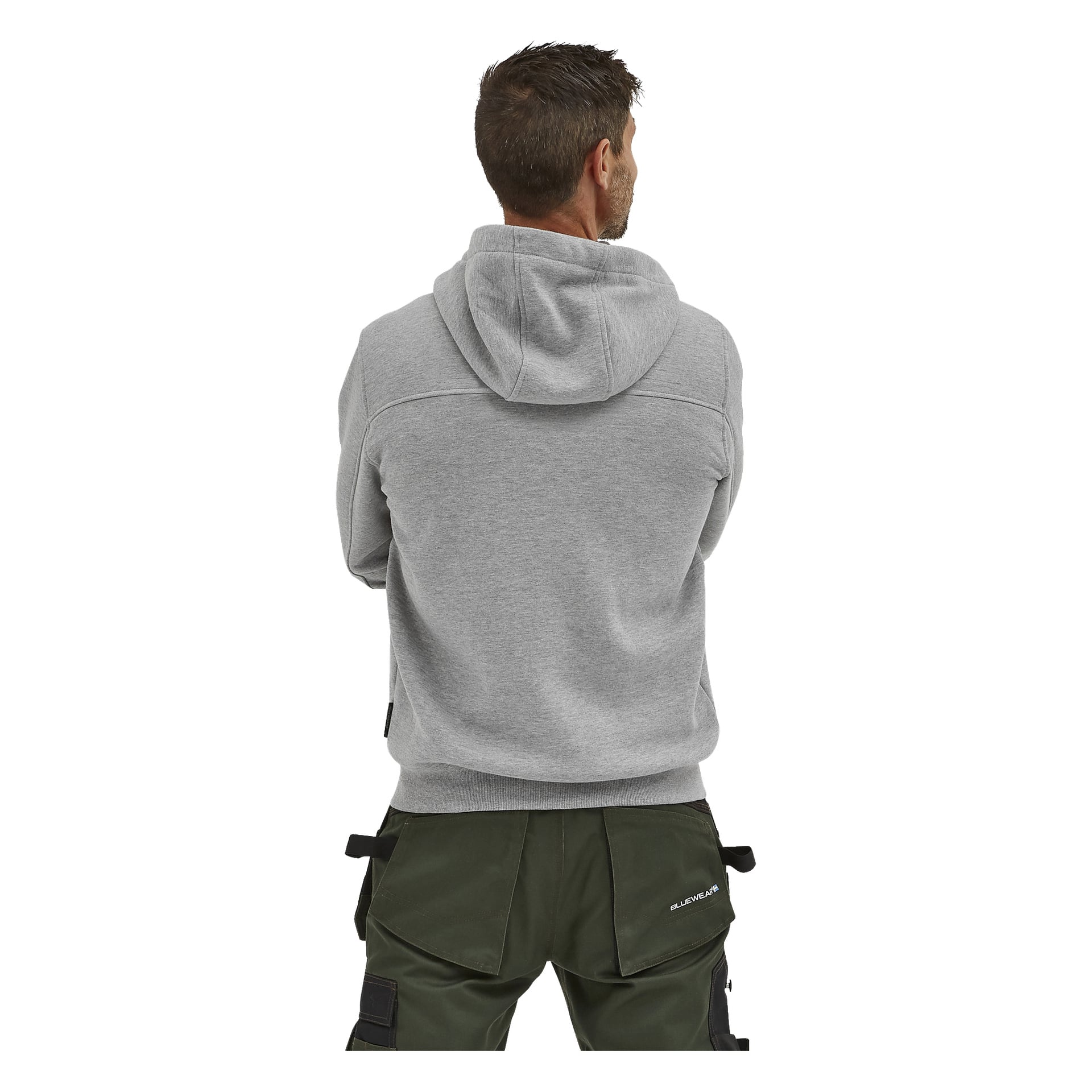 En man vänder blicken bort från kameran, klädd i en ljusgrå Bluewear herrhoodie Anders och mörkgröna arbetsbyxor med flera fickor och verktygsöglor. Hans huvud är försiktigt vänt åt sidan.