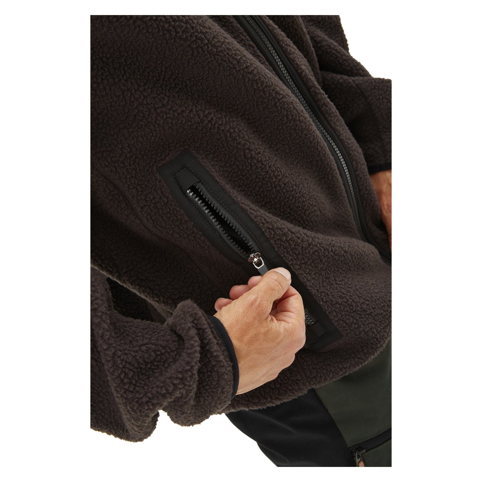 Någon håller på att dra ner dragkedjan på en mörkbrun Ljusdal Men's pile-jacka från Kayoba Outdoor. Bilden fokuserar på hand- och dragkedjan från midja till bröst, vilket betonar jackans texturerade fleecetyg.