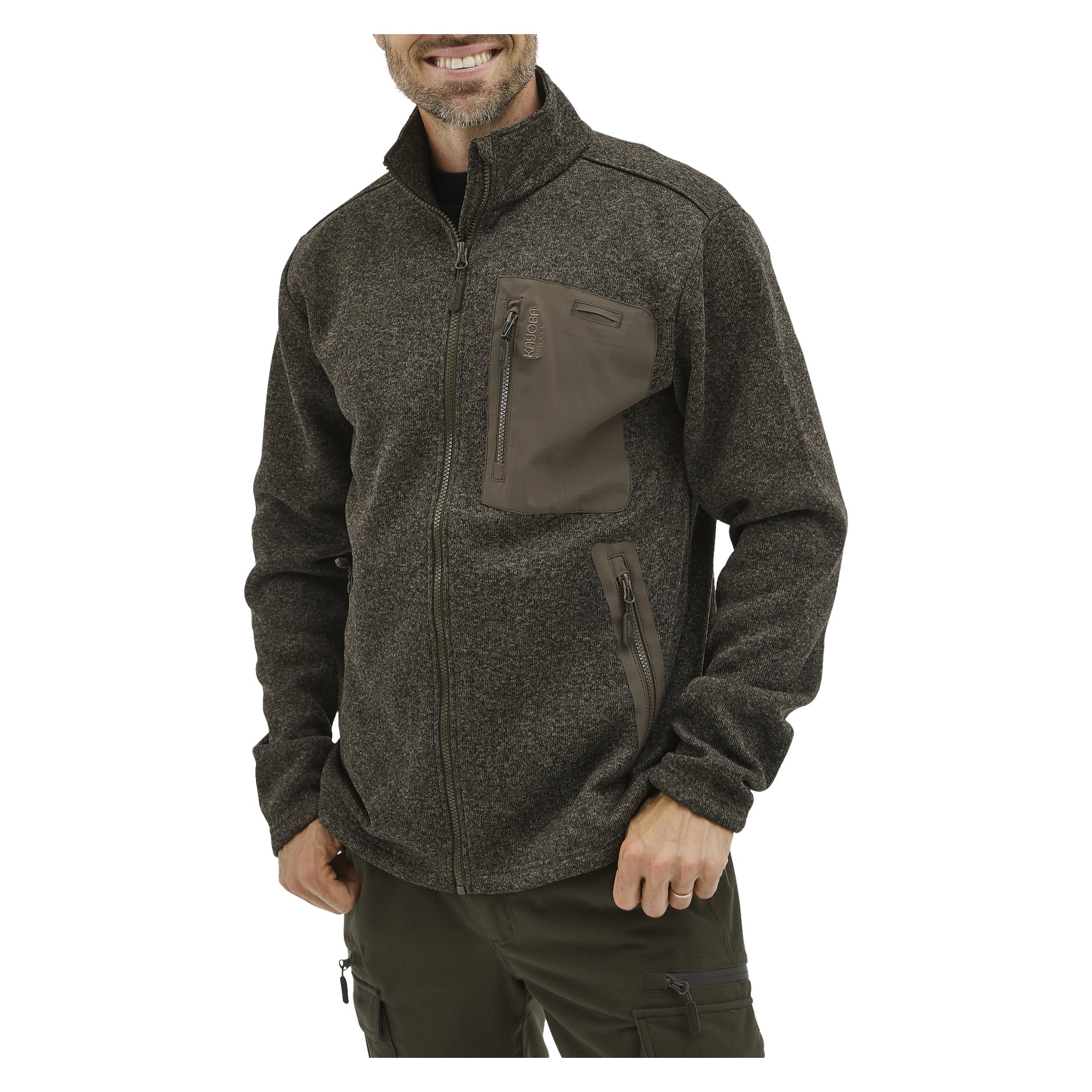 En man ler medan han bär Kayoba Outdoor Men's Grimsö fleecejacka, en mörkgrå dragkedja med dragkedja på bröst och sidoromor. Han står med ena handen i fickan och är klädd i mörka cargobyxor.