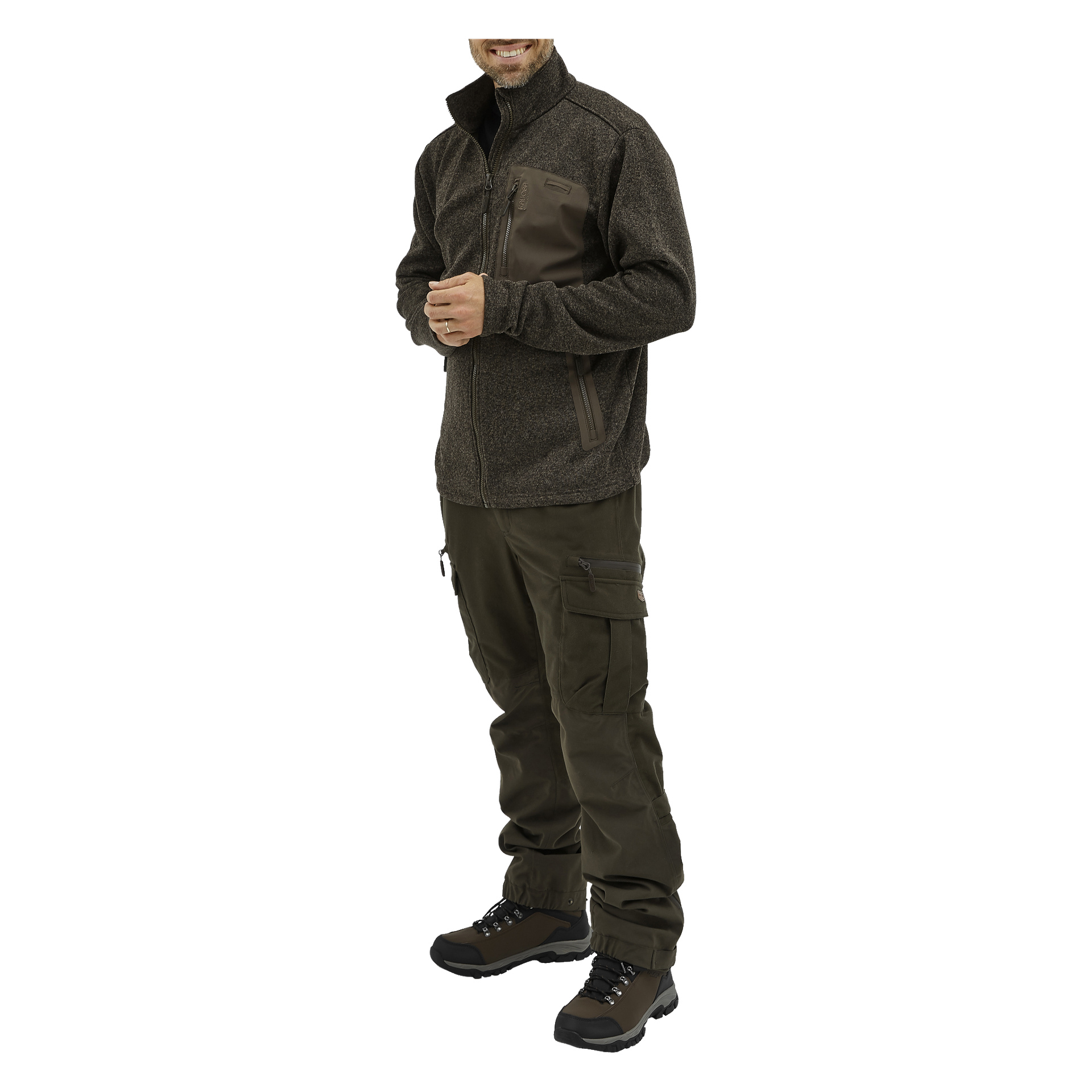 En person klädd i Kayoba Outdoor Men's Grimsö fleecejacka, olivfärgade cargobyxor och svarta vandringskängor står med ett leende. Deras hållning är avslappnad, en tumme vilar i fickan, och bara en del av ansiktet syns.