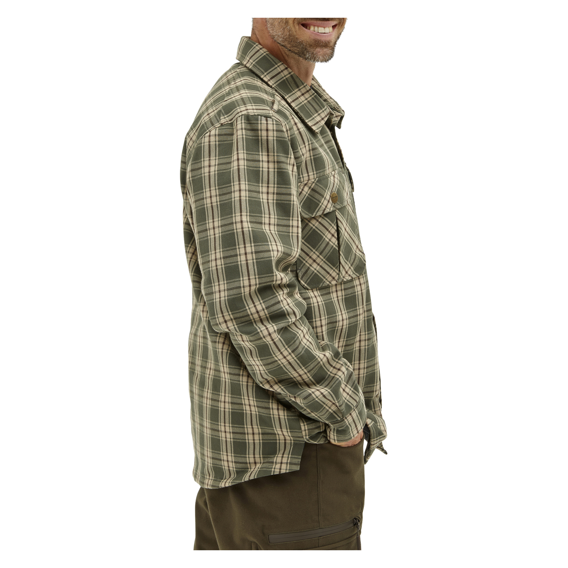 En person klädd i Kayoba Outdoor Windproof flanellskjorta från Grimsö, med grönt och beige rutigt mönster, tillsammans med mörka byxor, står i profil med ett leende och ena handen nedstoppad i fickan.