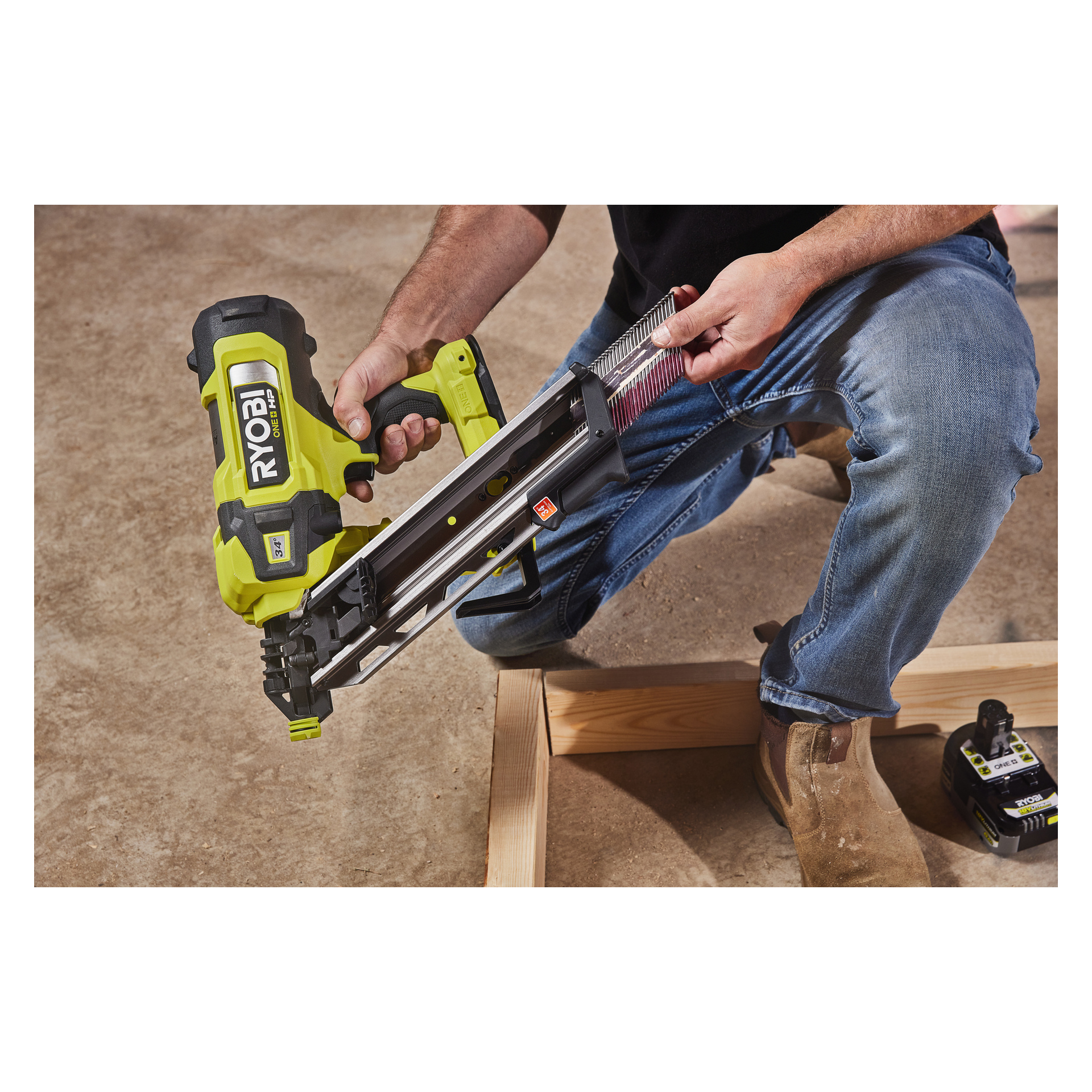 Joku työntää nauloja Ryobi One+ HP -akkukäyttöiseen naulapyssyyn RFN1834X-0 puurungon viereen betonilattialla. Erillinen paristo lepää lähellä, ja henkilö on pukeutunut mustaan paitaan ja sinisiin farkkuihin.