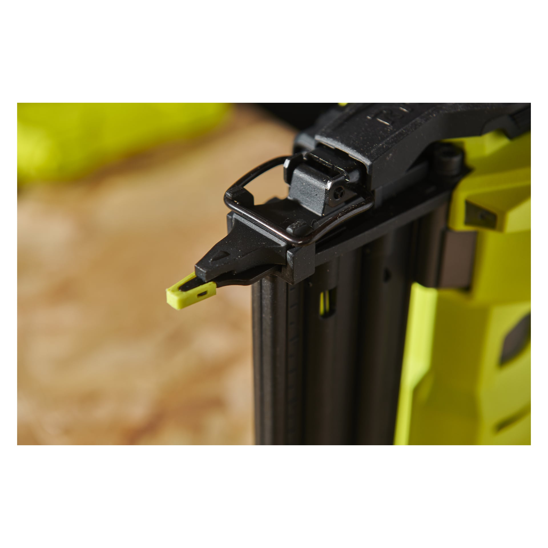 Detaljerad närbild av spetsen på Ryobi One+ HP AirStrike R18GN18X-0 brad-spikpistol, som framhäver dess mekaniska komponenter och en gul förlängning som sticker ut från änden, med bakgrunden mjukt ur fokus.